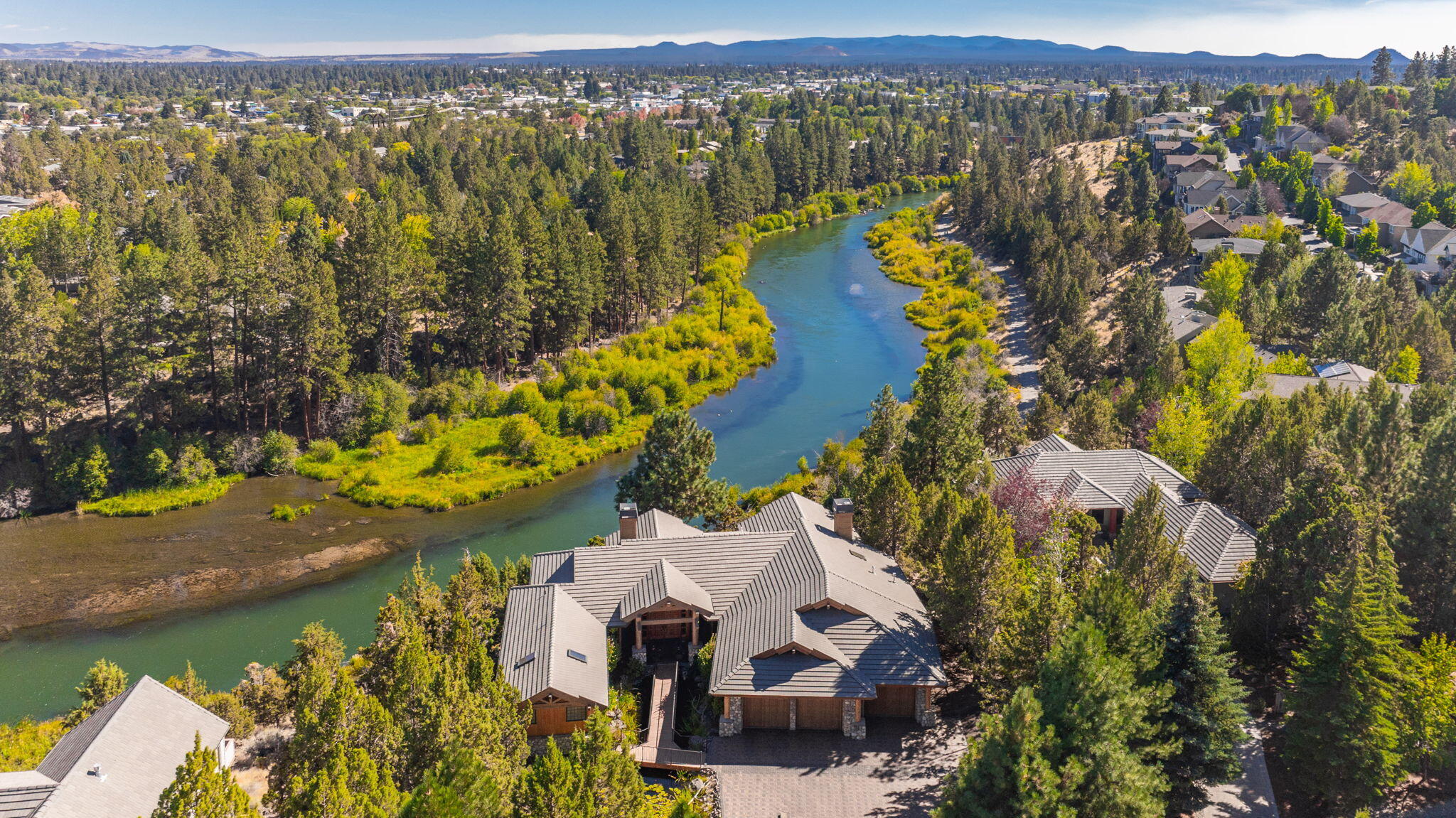 Nestled along the beautiful Deschutes in the heart of Bend, this majestic home features a serene setting yet close to all Bend has to offer. The custom, main level living masterpiece is a rare gem, thoughtfully designed & meticulously crafted. A dramatic cascading water feature guides you to the grand entry bridge. Enter to vaulted ceilings accented with log posts & rich wood finishes, creating a warm, inviting ambiance. The kitchen truly delivers, featuring an 8-burner gas cooktop, refrigerator, wine fridge, & ice maker—an entertainer's dream. Expansive windows frame tranquil river views, whether you're relaxing in the great room or unwinding on the  patios. The primary suite is a private retreat, complete with 2 walk-in closets, a generous jetted tub, & 2 full bathrooms beautifully updated in 2023. Enjoy the ultimate home theater, alongside a second primary suite, a full kitchen, & versatile flex space ideal for a third bedroom, office, or hobby room. All this plus a heated driveway