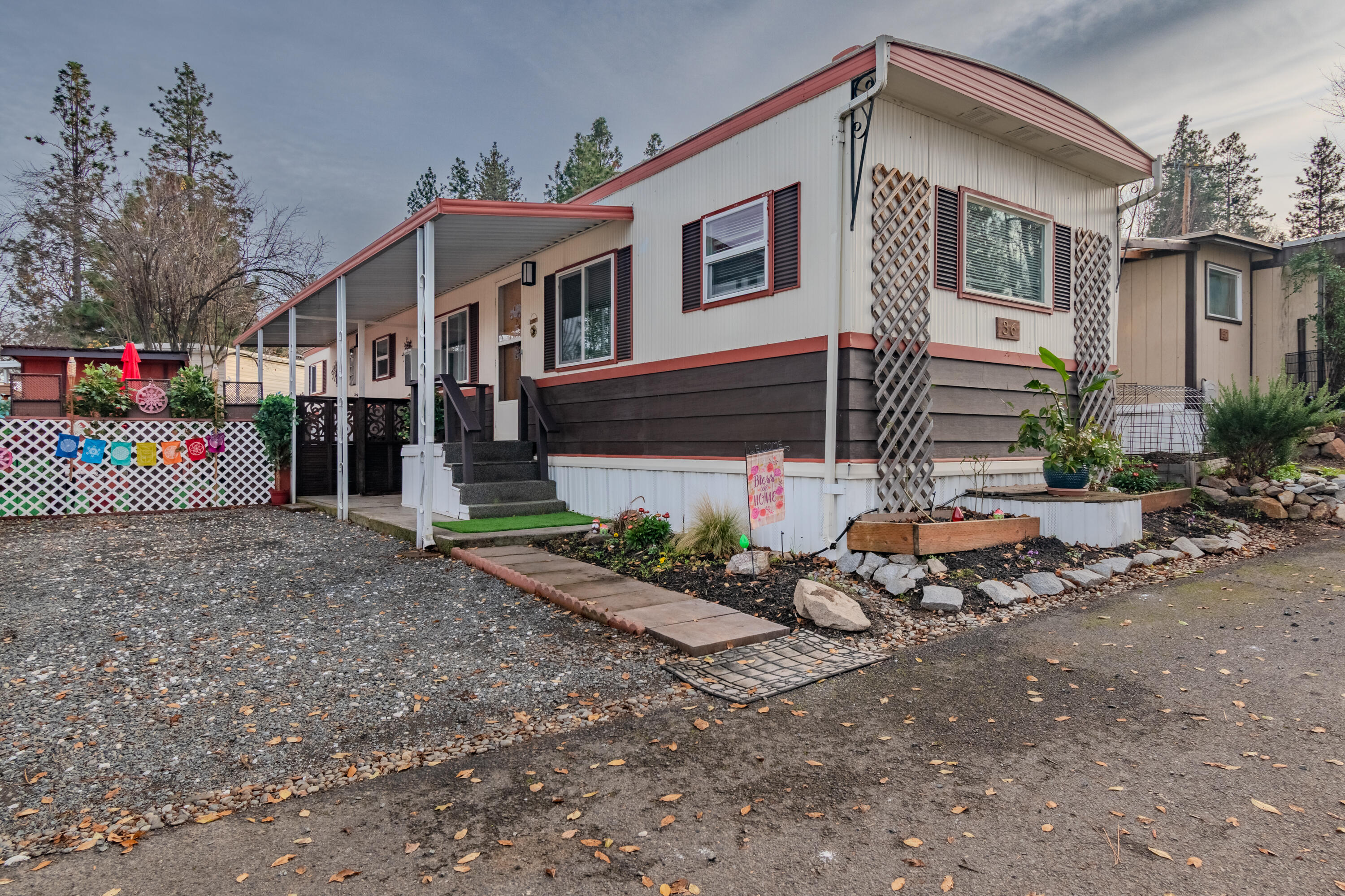 Welcome to Siskiyou Mobile Village on Ashland's south end—an all-ages community offering a mix of RV spaces and single-wide manufactured homes. Built in 1971, Space #36 has been thoughtfully improved by the current owner. Updates include new wood-laminate flooring throughout, fresh white interior paint, and refinished cabinetry, including the built-in china hutch in the living room. The home features vinyl windows, two window A/C units, refreshed skirting, and a charming decorative gate at the yard entry. A rare bonus in this park is the finished and insulated shed with washer/dryer hookups, although the park does have onsite laundry facilities. Architectural bump-outs in both the living room and primary bedroom create inviting, functional spaces that add character beyond what you typically find in a 744 sq. ft., 2-bed/1-bath home. The gravel driveway can accommodate multiple vehicles depending on size, with potential to expand if desired.