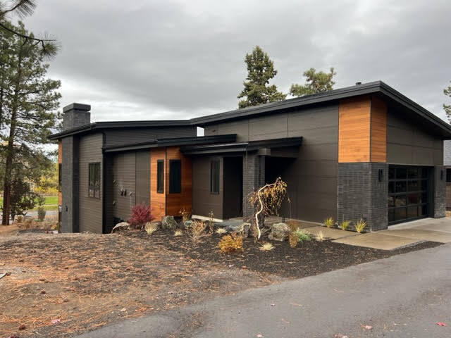 Nestled along Farewell Bend Park and the Deschutes River, this modern two-story house with industrial finishes is a stunning blend of contemporary design and natural beauty, its sleek lines, steel accents, and large windows offer a lovely glimpse of the breathtaking park and river view beyond. The house is an architectural masterpiece with clean lines, and a combination of materials that create a modern industrial aesthetic. The facade is covered in a combination of dark gray and black, coupled with rustic cedar. Large expanses of glass offer a seamless connection between the interior and the picturesque river park. The interior design embraces the upscale theme with a neutral color palette, accented by warm wood and metal finishes. The living room features a floor to ceiling fireplace,  oriented towards the large windows, framing the deck and views. This modern two-story home with industrial finishes seamlessly blends contemporary design with the beauty of its natural surroundings.