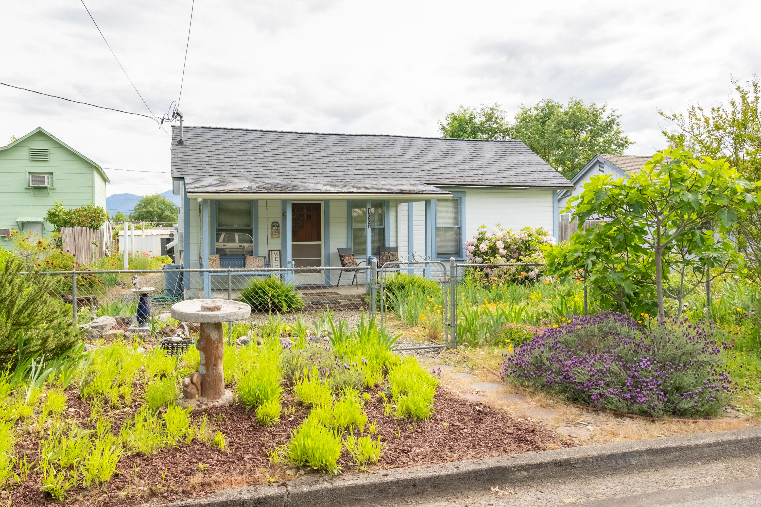 Located not far from the center of Grants Pass' historic district, this charming turn-of-the-century home is built on a solid concrete foundation. Recent updates include new plumbing from the house to the street sewer system. This adorable cottage is comfortable and move-in ready, making it a perfect starter home, Airbnb, or rental property. The primary bedroom and living room feature tall ceilings, while the spacious full bathroom includes a bathtub and shower combo. When you enter the kitchen, you'll feel as though you've stepped back in time to a homestead on the prairie, complete with ample cupboards and a central cutting table. The large back porch boasts bright windows and a utility sink, perfect for everyday use. Outside, you'll find an old-fashioned clothesline, a fully fenced yard, a delightful gazebo, and a carport, along with an array of colorful flowers that have been planted over the years. Sitting on the front porch in this quaint neighborhood is truly a pleasure