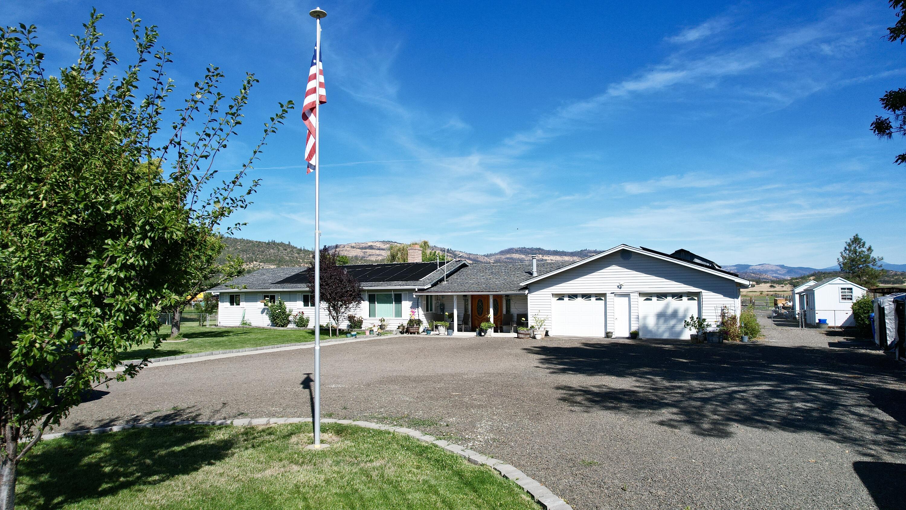 Enjoy country living with stunning mountain views from this versatile 4.92-acre property featuring a 3-bedroom, 2-bath, 1,694 sq. ft. home with a sunken living room, family room with fireplace, newer appliances, granite kitchen countertops, tile backsplash, hardwood flooring in kitchen, pantry, and a large concrete patio overlooking an in-ground solar-heated pool. Additional amenities include a detached office/storage space, an oversized 2-car garage (868 sq. ft.), a mini barn, a 30x40-animal barn with stalls and hay loft, several outbuildings, raised garden beds, greenhouse, and fenced and cross-fenced areas with invisible fencing in the front yard—ideal for animals, gardening, or simply enjoying the peaceful setting.