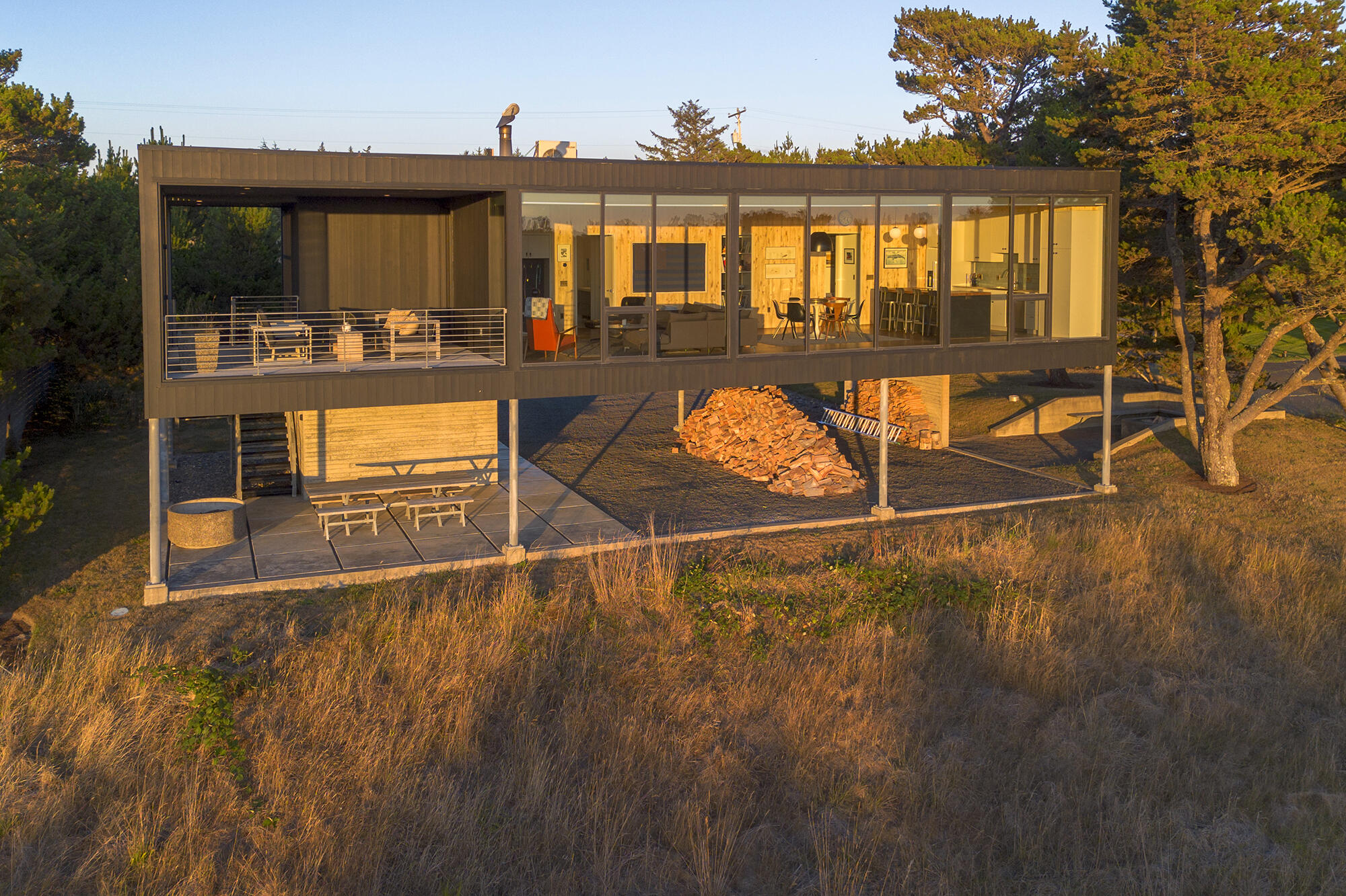 Elevated modern beach retreat. Designed by Pacific Northwest architect Paul McKean, this home in beautiful Surfpines highlights the panoramic view of the Pacific ocean and natural landscape with western facing floor-to-ceiling windows. An expansive great room combining living, dining and kitchen with adjacent patio. Thoughtful covered parking with additional outdoor living area. Cedar siding and ceilings in all outdoor areas with board form concrete storage room and fire pit with built in benches. These features add to the efficient layout of this one acre, one-of-a-kind property. Primary bedroom with attached bathroom, large bunk room with seating area and second guest bedroom and bathroom make for a comfortable coastal refuge.