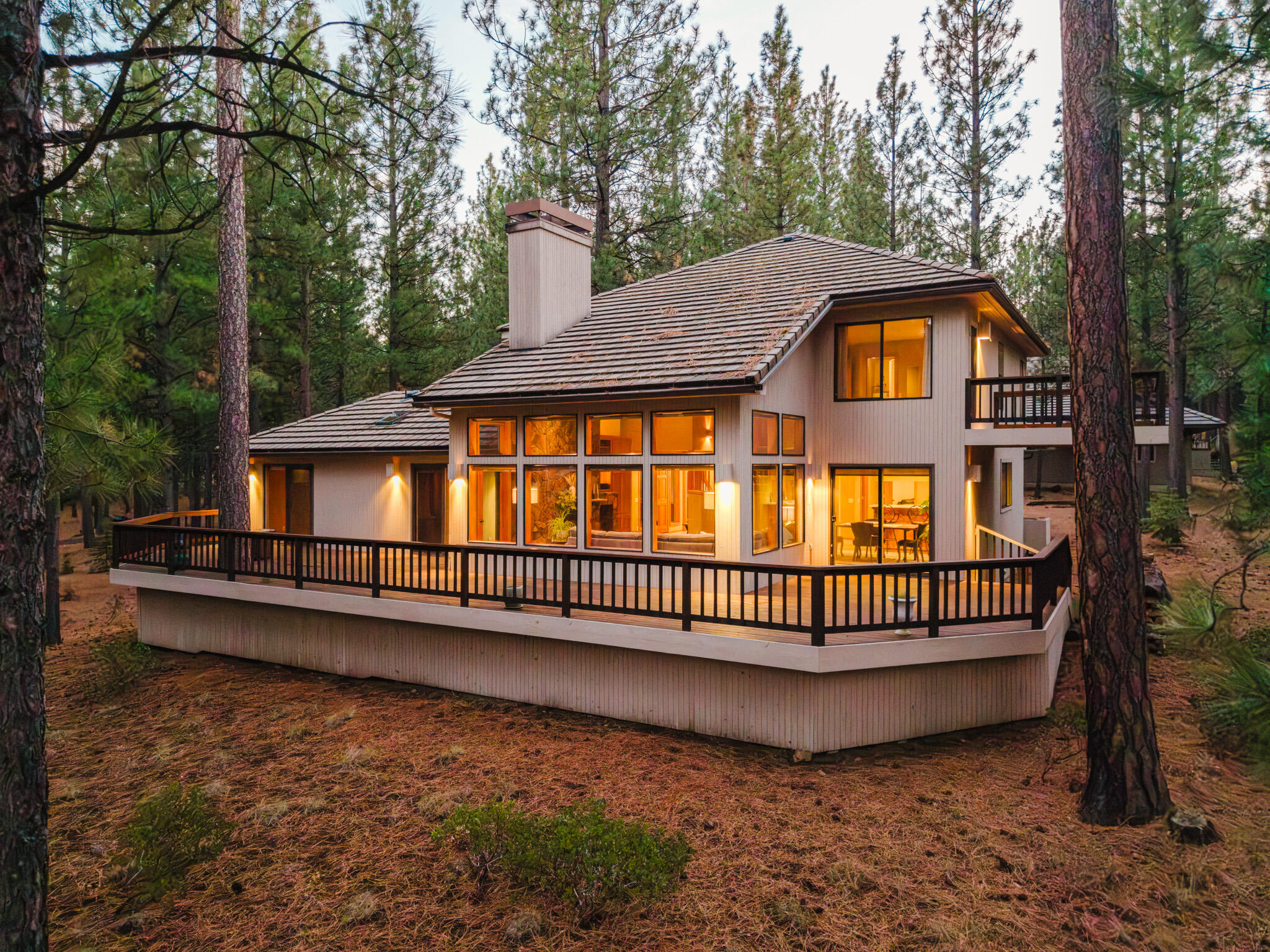 A peaceful, serene retreat on the Ranch perimeter, this lovingly updated home features a versatile, light-filled floor plan and design. Tucked away on lightly traveled roads and bordering common land, it offers quiet seclusion while just a short stroll from a Ranch pool and amenities. Expansive windows create a seamless indoor-outdoor connection. The vaulted living room, with grand floor-to-ceiling slate fireplace and wood-burning insert, invites cozy gatherings, while the kitchen with stainless steel appliances, rosewood island with induction cooktop, quartz counters, wet bar, and breakfast bar is perfect for entertaining. Two guest bedrooms down a window lined hallway open to the main deck, and a bonus room provides flexible space. Upstairs, a private owner's suite with deck and a versatile library/office overlooks the living room and tree-filled views. Updated baths, heat pump, tile roof, double garage, and ample storage make it move-in ready for enjoying Black Butte Ranch living.