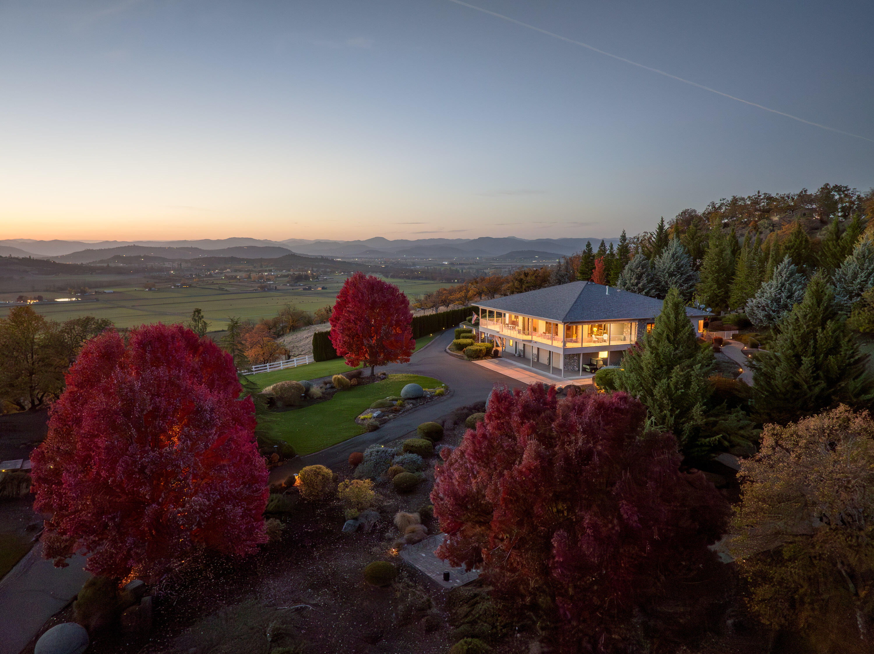 A distinguished country estate where timeless craftsmanship meets the beauty of Southern Oregon's landscape. Set amid 16 acres of lush, mature landscaping, this 4,810± sq. ft. residence offers refined single-level living with a lower-level guest suite. The home's warm cherry hardwood floors, coffered ceilings, and custom millwork complement expansive windows framing sweeping mountain and valley views. The chef's kitchen features granite surfaces, a large island, walk-in pantry w/butlers sink, and flows seamlessly into a dining space and elegant living room centered around a propane fireplace. French doors open to a private atrium with tranquil waterfall and outdoor kitchen just outside, perfect for entertaining or quiet reflection. Thoughtful design extends to three primary suites (two on the main level), zoned climate control, elevator access to the finished 3-car garage, and a wraparound porch overlooking manicured gardens and the serenity of this remarkable property.