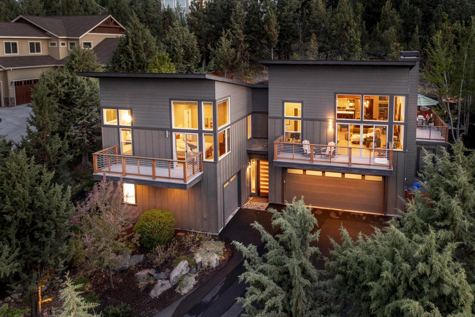 A light and airy contemporary Earth Advantage home tucked into the hillside in Awbrey Park, featuring a reverse-living layout with soaring 20' ceilings, multiple decks and patios, and a flat and fenced back yard sanctuary.  Here, you will find a spacious greatroom that connects nicely with the formal dining space, modern kitchen, and private butler pantry - all ensconced in windows and light from every direction. Three main floor bedrooms, plus an office, ensure room for all. On the garden floor, find a full suite with sitting space and wet bar with beverage fridge - perfect for guests or generational living.  Storage is endless with three garage spaces, an entry mudroom, and plenty of closets. Additionally on the ground floor, enjoy a private fitness nook and built-in sauna. Solar panels are included in the sale, and the driveway is heated!