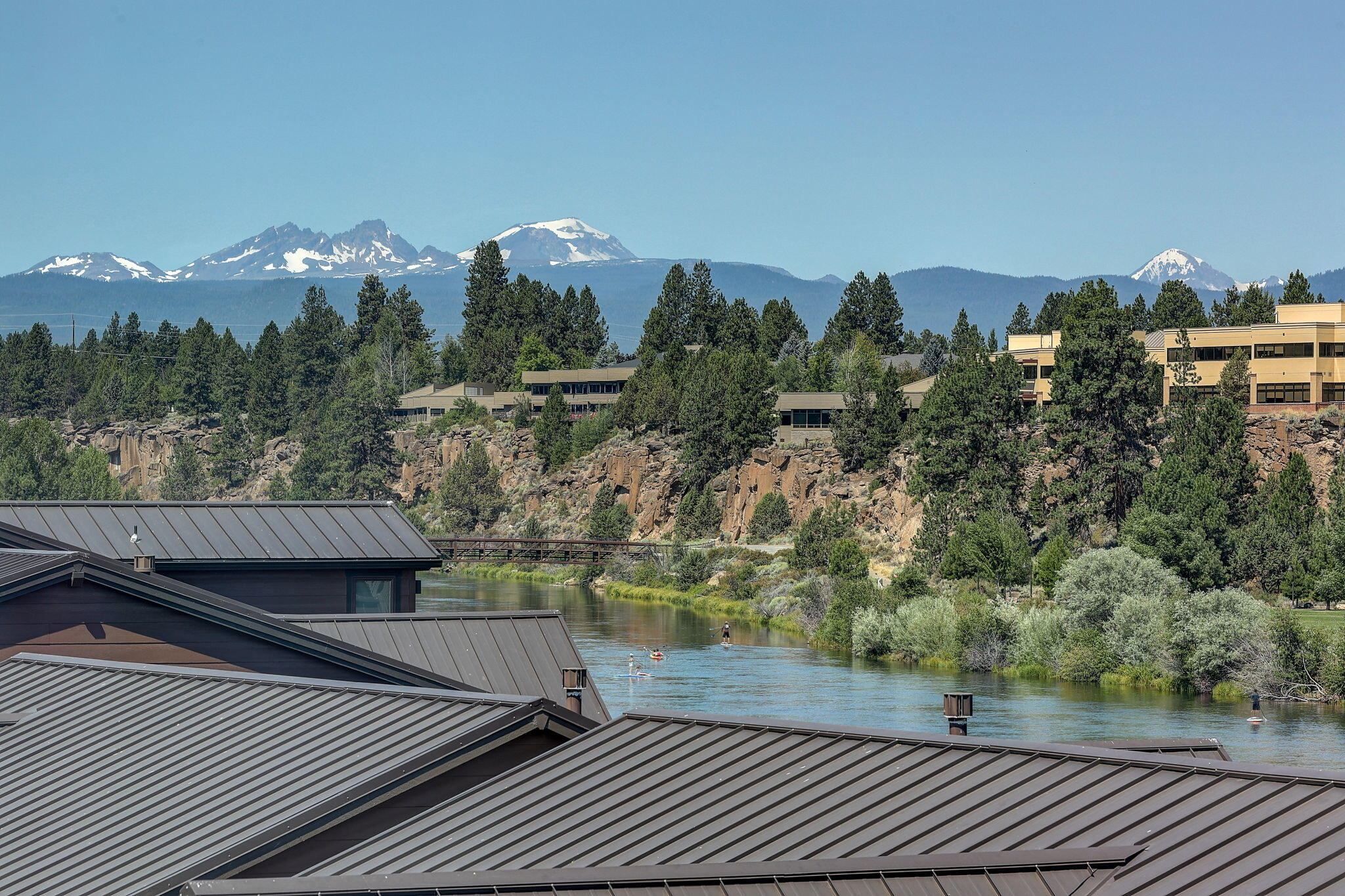Elegant townhome with breathtaking river and mountain views, situated in the prestigious Deschutes Landing neighborhood in the heart of the Old Mill District. Just steps from the Deschutes River, dining, and shopping, this home offers the perfect blend of convenience and luxury. The spacious, open-concept floor plan is designed for entertaining, featuring a generous deck off the living area, a cozy office nook, and central A/C. The gourmet kitchen showcases top-of-the-line appliances and custom finishes throughout. The expansive primary suite includes a walk-in closet and a beautifully upgraded en-suite bathroom with a designer-tiled glass walk-in shower and custom lighting. A rare three-car garage with a workshop area provides ample space for storage, outdoor gear, and more. Enjoy a private, fenced patio and backyard area.  Short-term vacation rentals are allowed and city permit not required. Sold Turn Key Furnished.