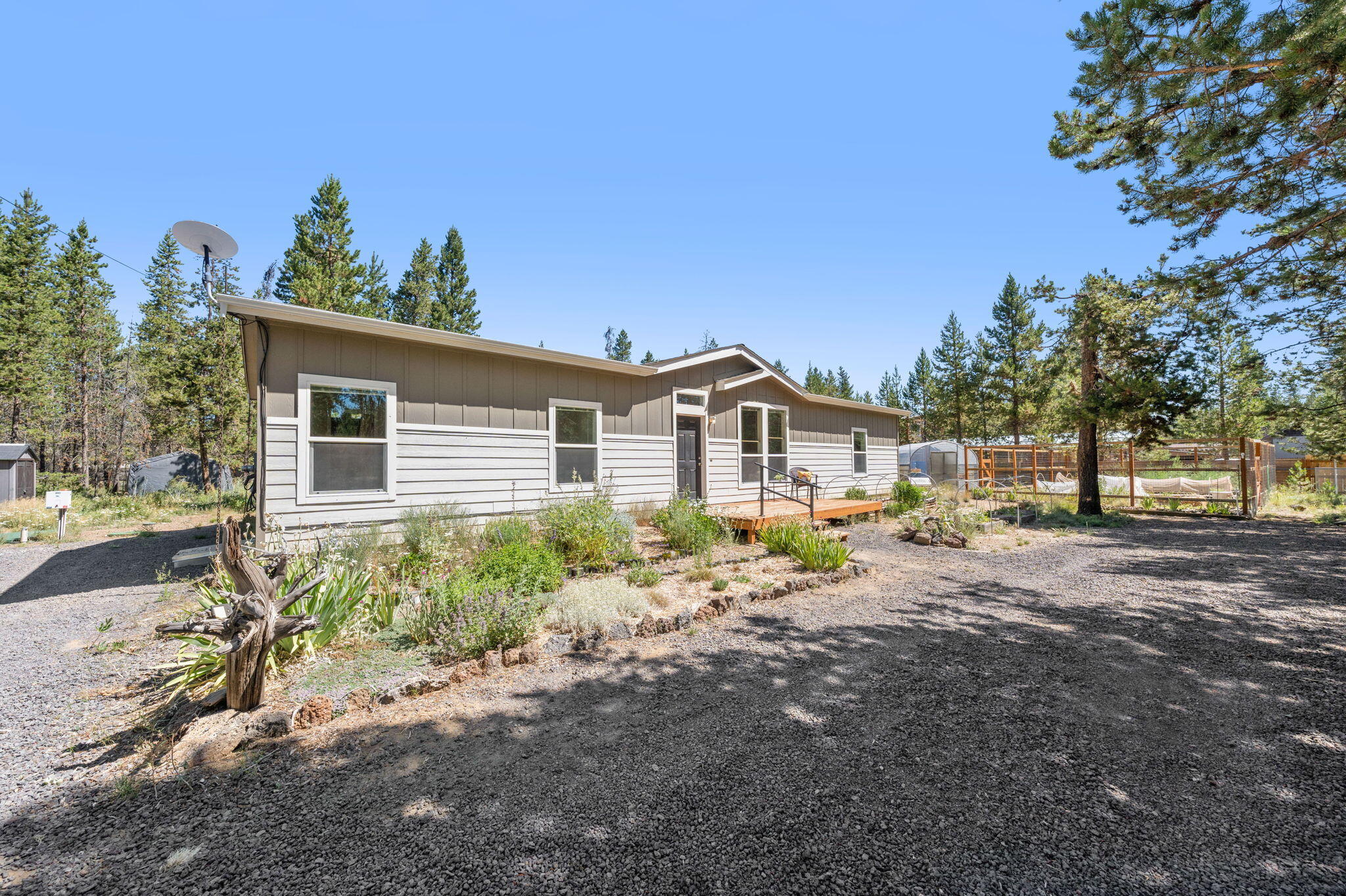 Charming 3 bed, 2 bath 2019 double-wide on concrete foundation, generator ready (generator included) on 1.05 acres with upgrades. Situated at the end of a quiet road on a corner lot. Each bedroom features a walk-in closet. The primary suite includes a ceiling fan, walk-in tile shower with glass enclosure, double vanity, and enclosed water closet w/additional cabinets. Spacious kitchen with large island, knotty alder cabinets, walk-in pantry with motion-sensor lighting, 2023 induction range, fridge, microwave, and dishwasher. Additional features include updated ceiling fans, bathroom fixtures, window fans, window AC, blinds, property cameras, window shelves, crown molding, and a weather station. Electric furnace, dedicated laundry room with shelving. Enjoy outdoor living with front and back decks, 7-ft fencing around raised beds, greenhouse, compost bin, EV charger, sheds, and a tarp shelter. Surrounded by mature pines—move-in ready and full of extras!