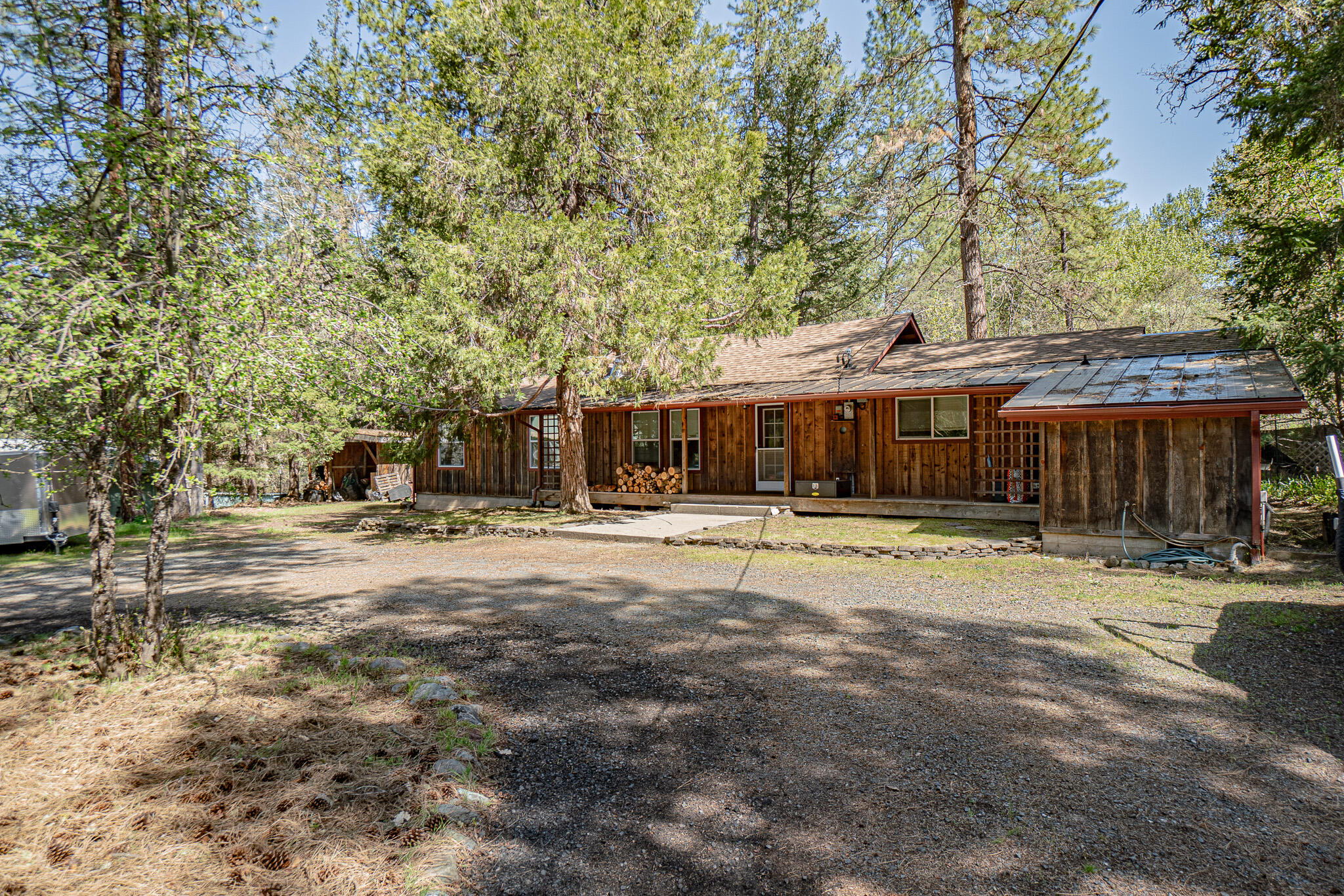 Charming Country Retreat on Nearly 1 Acre with Workshop & Plenty of Privacy
Located in a sought-after neighborhood, this beautiful bat and board wood-sided home sits on just under one private acre, offering the perfect balance of country living while remaining conveniently close to everything you need. The property features a spacious backyard, ideal for outdoor entertaining, with a large deck perfect for relaxing or hosting guests, along with a chicken coop for your farm-fresh eggs. For added convenience, there's extra covered storage for firewood and a circular driveway for easy access.
Inside, the home is warm and welcoming, with a large kitchen/dining area perfect for meals with family and friends, and a laundry room for added practicality. The spacious living room, with its vaulted ceilings, offers a light-filled and open atmosphere. This cozy home includes two bedrooms and a well-appointed bathroom, with stunning bamboo and tile flooring throughout that adds a modern touch.