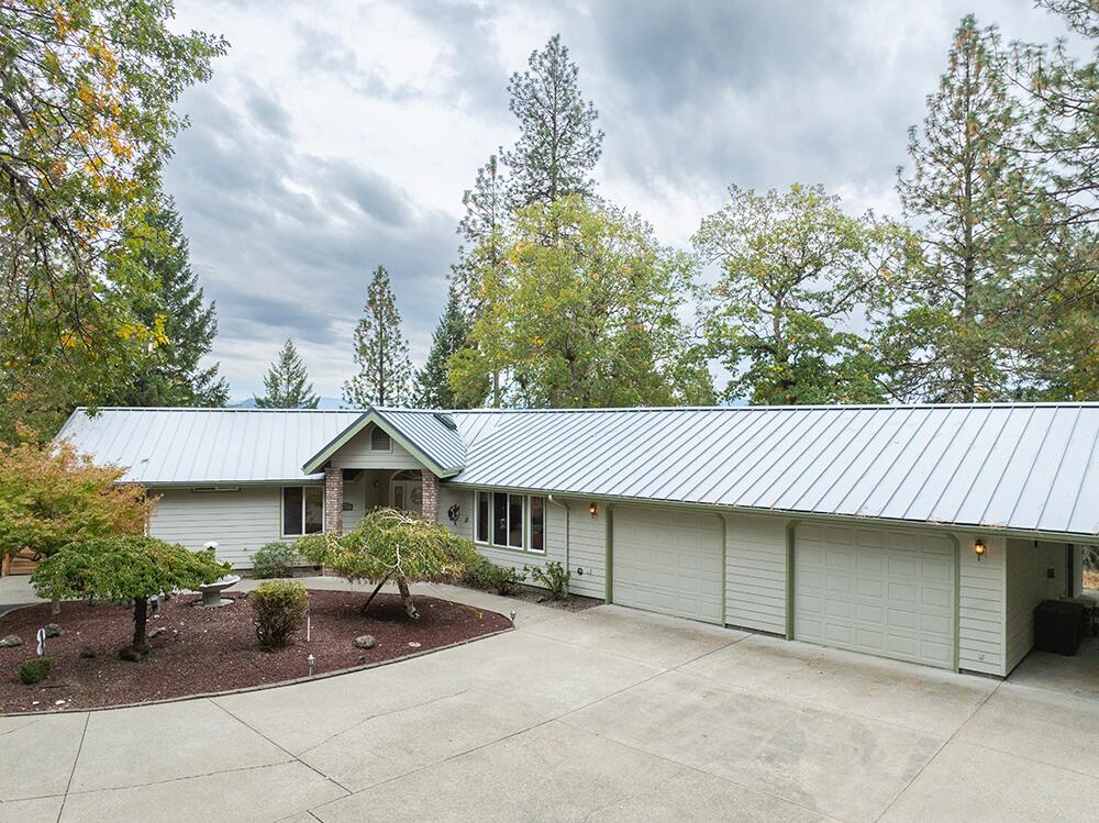 Discover your private retreat on 10 gated, peaceful acres with lovely forest & mountain views! This beautiful single-level 3 bed, 2 bath home offers 1922 sq ft of comfortable living with vaulted ceilings, skylights, and a bright great room design centered around a cozy wood stove. The spacious kitchen features a large breakfast bar, lots of storage and prep space, which opens to a generous dining area—perfect for entertaining. The expansive primary suite provides a walk in closet, dual vanities, lots of light, and relaxing mountain views. Enjoy outdoor living on the wrap-around deck with space for multiple gathering spots overlooking the serene landscape. Car enthusiasts will love the 4-car attached garage, carport, and impressive 1400 sq ft detached 3-bay garage/shop with RV parking and full bath. Additional highlights include a large laundry room and paved, gated driveway. A rare blend of space, comfort, and country charm just minutes from Grants Pass amenities!