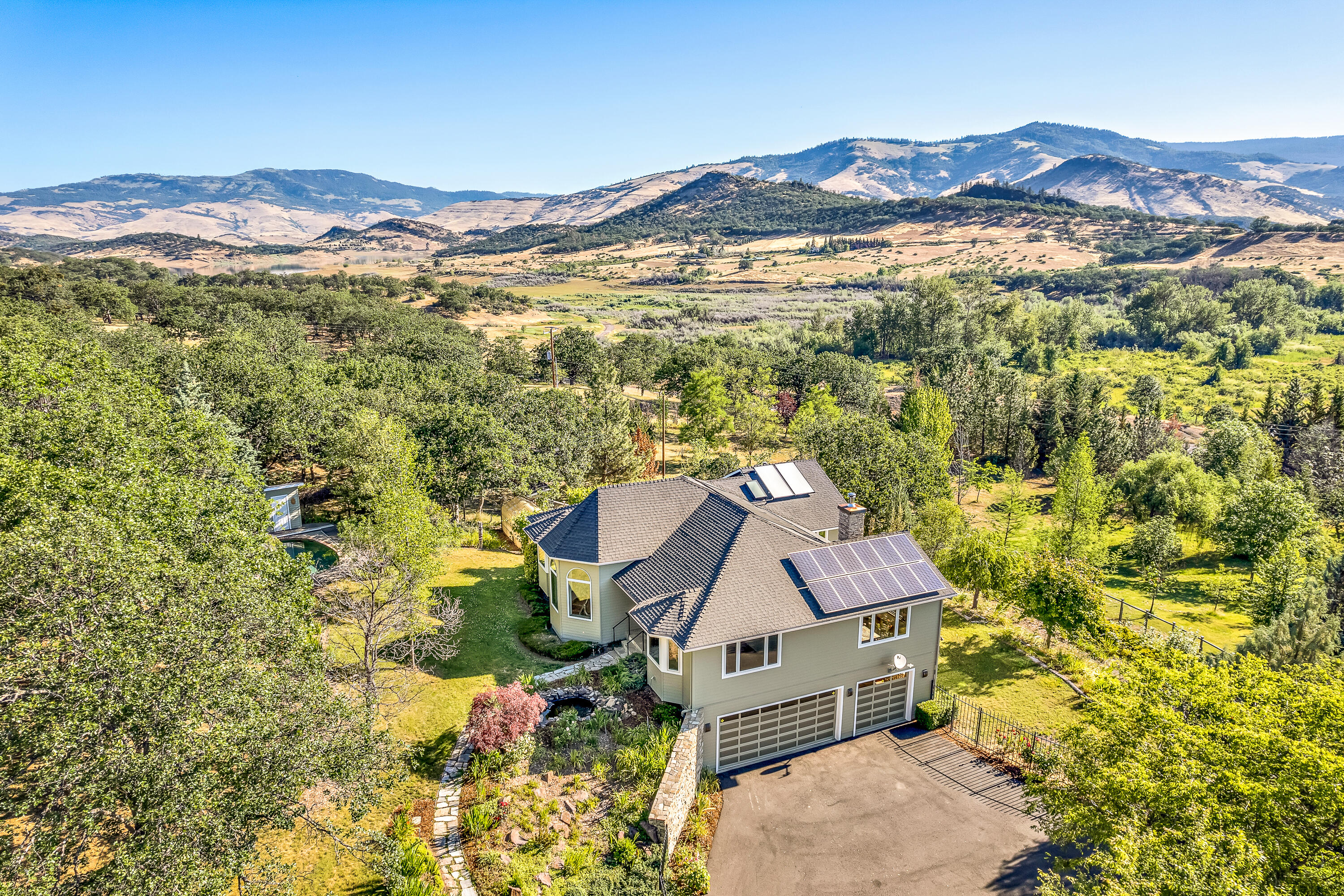 Spacious custom view home on acreage with swimming pool and mature landscaping near Emigrant Lake — just 8 miles from downtown Ashland! Main level with solid oak floors and fir doors, double-paned casement windows, vaulted living room with stone fireplace surround, parlor sitting room or office, formal dining with sliding glass door to balcony, kitchen with granite counters and island, informal dining or breakfast nook with gas fireplace, composite deck with BBQ hookup, half-bath, laundry room, primary bedroom with deck access, and full ensuite bathroom with radiant-heated marble floors, two closets, double vanity, soaking tub, and shower. Curved staircase to lower level with wet bar, two spacious bedrooms, full guest bathroom, and three-car garage with workshop. TID rights with sprinkler and drip irrigation, 2-kW solar array, oak and fruit trees, greenhouse, ~950 SqFt fenced garden, koi pond, and approximately one fully-fenced acre around the home. Inquire with agents for details!