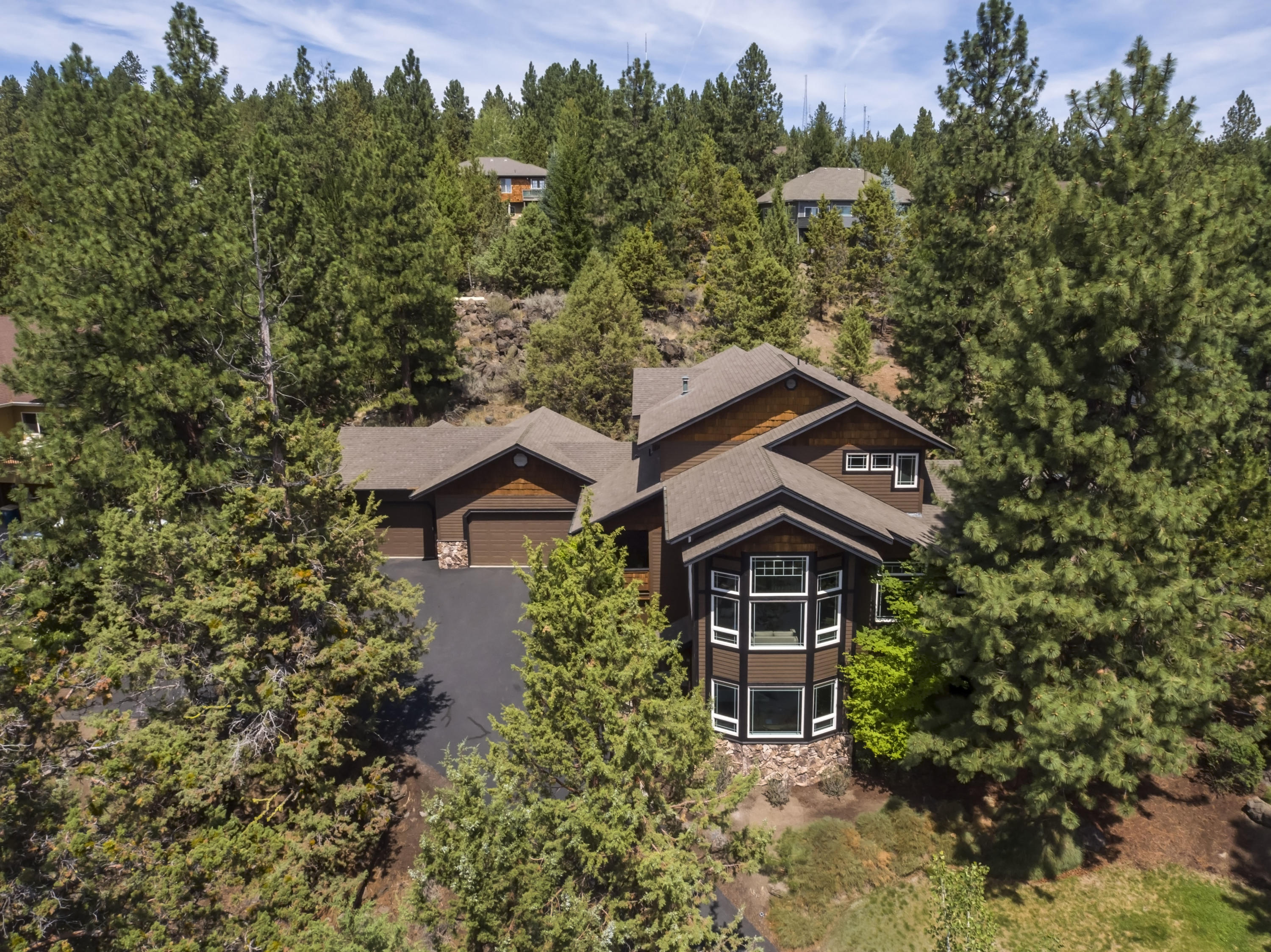Located on the southern flank of Awbrey Butte, this inviting home is nestled in the trees yet designed to highlight the views and lights of the city and mountains to the south. Light and bright, the open floor plan flows from the entry to the living spaces and central kitchen. High ceilings and many windows bring the outside in. The family room featuring a beautiful stacked stone fireplace, opens to a protected front deck and rear outside living area. The spacious primary suite on the main level has a fireplace & access to the patio & hot tub. Upstairs there are 2 bedrooms & bathroom, plus a bonus room/office/4th bedroom. On the lower level the spacious office, with separate exterior entry, could also serve as guest room. Easy access to the huge unfinished basement. Attached 3 car garage, over 1000 sq ft, also offers lots of storage. Private and peaceful, the ½ acre retreat includes natural elements, a cascading water feature, lawn front and back, and frequent visits from wildlife!