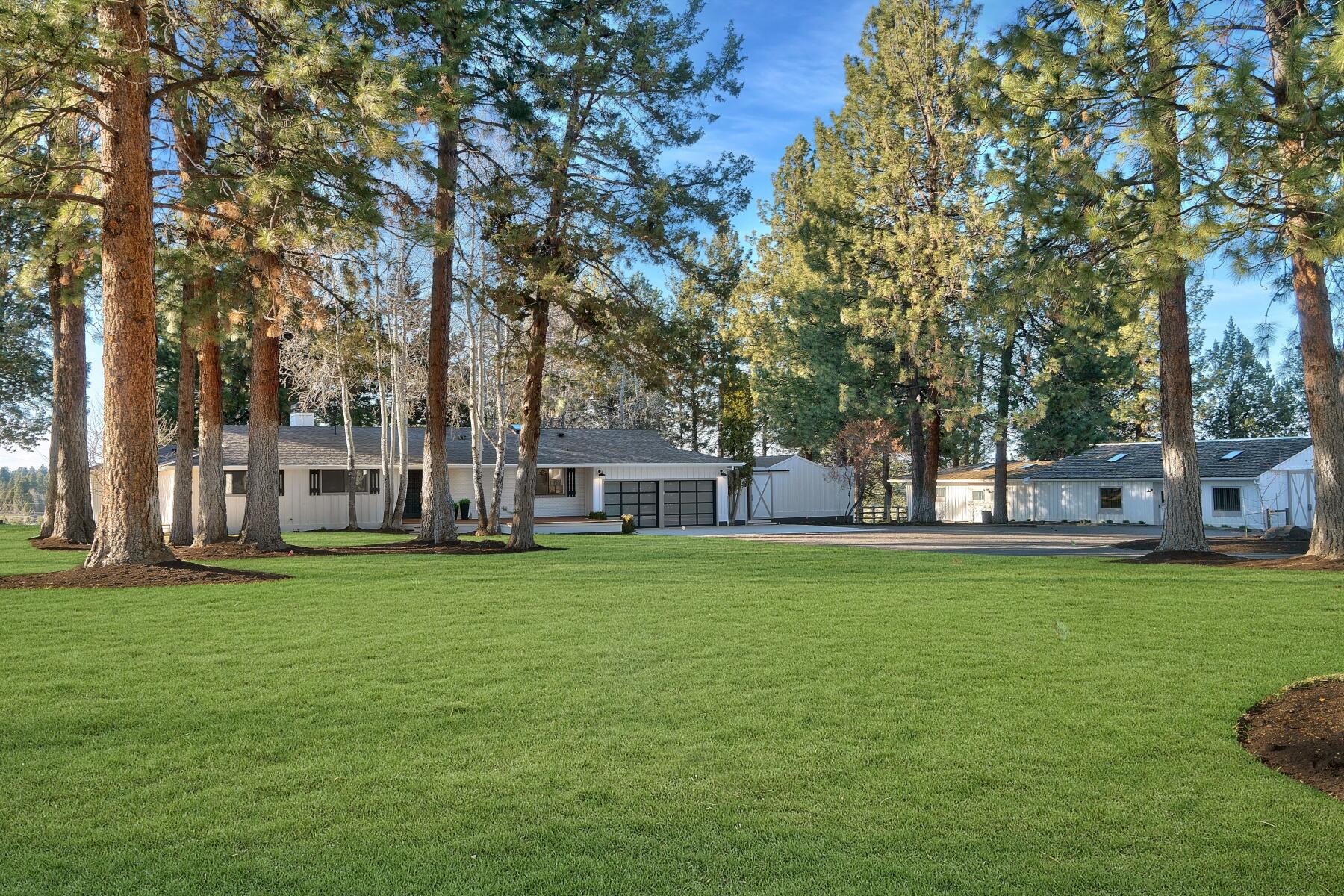 As you drive down the tree lined driveway and nestled among towering ponderosas on 4.5 pristine fenced acres with Cascade Mountain views, complete with a single-level mid-century modern farmhouse and 7 stall barn, both combining classic charm with modern comfort. Boasting 3 bedrooms, 3 bathrooms, and spanning 2575 sq ft, this home has been carefully updated to welcome in abundant natural light while being surrounded by the peaceful ambiance of mature trees, irrigated pastures and mountain views. Step outside onto the nearly 3,000 sq ft rear deck and relax with friends and family after a day of making cherished memories in beautiful Central Oregon. Equipped with 3.15 ac of irrigation, 7-stall barn, and additional outbuildings, this property is a dream for equine enthusiasts, car collectors and hobbyists, offering a blend of rural tranquility and contemporary conveniences. Adjacent parcels at 60445 & 60559 Tekampe also available separately or as a multi parcel estate with farmhouse.