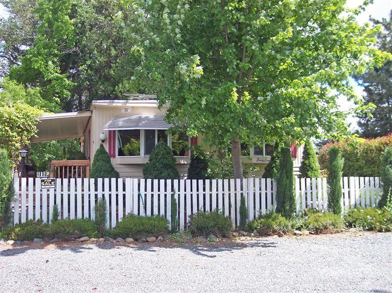 This home is a very comfortable place; inside and outside! It's really a spacious double-wide mobile home with a variety of upgrades in the best mobile park in Southern Oregon. Circle Tree Mobile Park and Ranch offers the least expensive space rent at $270/mo., including water, sewer, and trash. This area has a country-feel in what looks like a country, treed lane with mobile and manufactured homes here and there along it. This home is toward the end of the country lane with white picket fence (completely fenced in), quite a bit of privacy and lots of flowers. The home features 2 bedrooms, 1.5 baths, a convenient kitchen with range/oven and dishwasher and two great bay windows in front. There is a beautiful deck at the front door and a garden area behind continuing all the way around the home. Across from the deck is also a detached carport and shop. This home is move-in ready. Come take a tour and you'll want to stay.