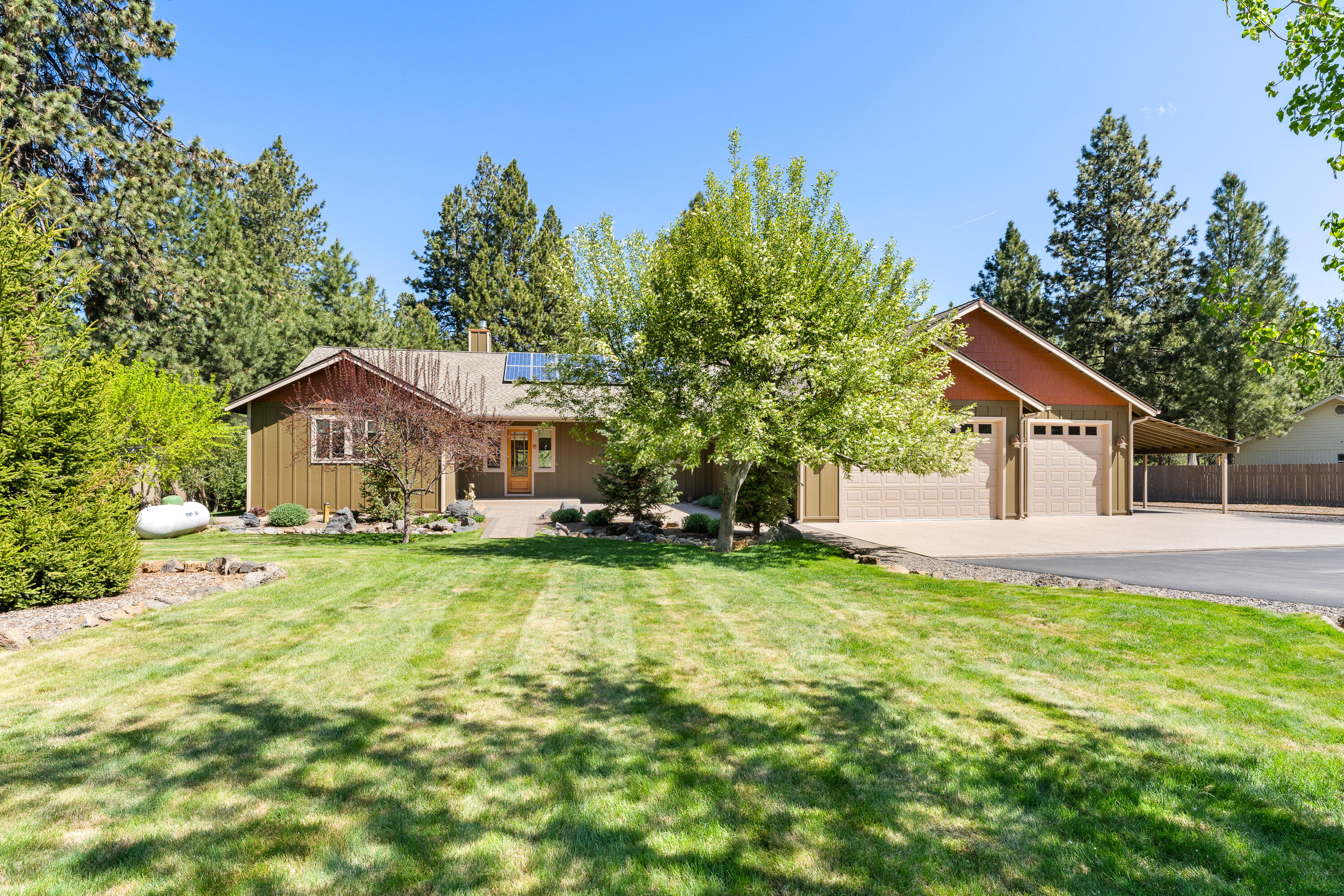 Situated on 1.34 acres, this meticulously maintained residence offers exceptional privacy, numerous upgrades and energy efficiency. The park-like, fully fenced and gated property has been thoughtfully landscaped for year-round enjoyment. Just inside the entry, a vaulted great room welcomes you with a gas fireplace, built-in shelving, and rich hardwood flooring. The chef's kitchen boasts stainless steel appliances, an expansive breakfast bar, and a walk-in pantry, all overlooking a spacious dining area. The west wing of the home includes two guest bedrooms, a bathroom, and an office, while the east wing features the primary bedroom suite and a massive bonus room. An oversized 3-car garage with utility sink, a carport, and 30-amp RV plug provides ample space for projects and parking. Solar panel energy production, a new 50-year roof, and fresh exterior paint make this home move-in ready—offering both a peaceful retreat and a highly functional homestead.
