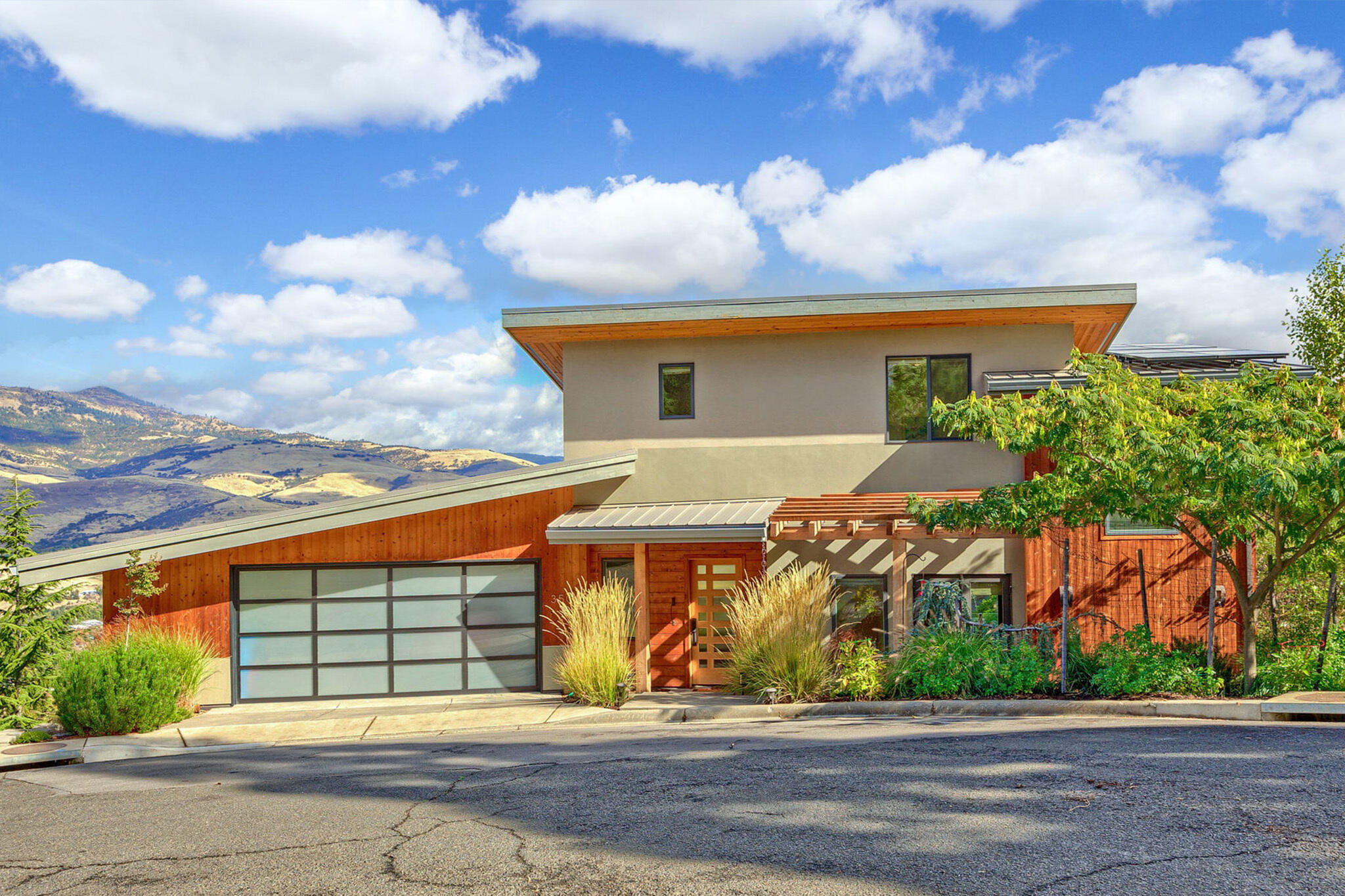 This 2016 Carlos Delgado designed hilltop retreat is a contemporary masterpiece. Efficient and beautiful, the design driver for this custom home was to capitalize on extravagant views. Built across three levels, this 2481 SF, 3bed/2.5bath home has great separation of space. On the main level, a cook's kitchen with granite counters and Fisher Paykel appliances, living room with stucco surround gas fireplace, office nook, and dining area. NanaWalls expand onto a covered deck for true indoor-outdoor living. The upper primary bedroom includes a lovely en-suite with soaking tub, heated tile floors & walk-in closet. Lower level includes 2 beds/1 bath/ & living area. Dynamic views grace the 3 terraced decks. Generous sloping lot with low maintenance landscape. 2 car garage, plus large basement space provide storage. Grid-tied rooftop solar array. Quality construction and attention to detail has resulted in this uniquely warm, modern home on a quiet cul-de-sac close to downtown Ashland.