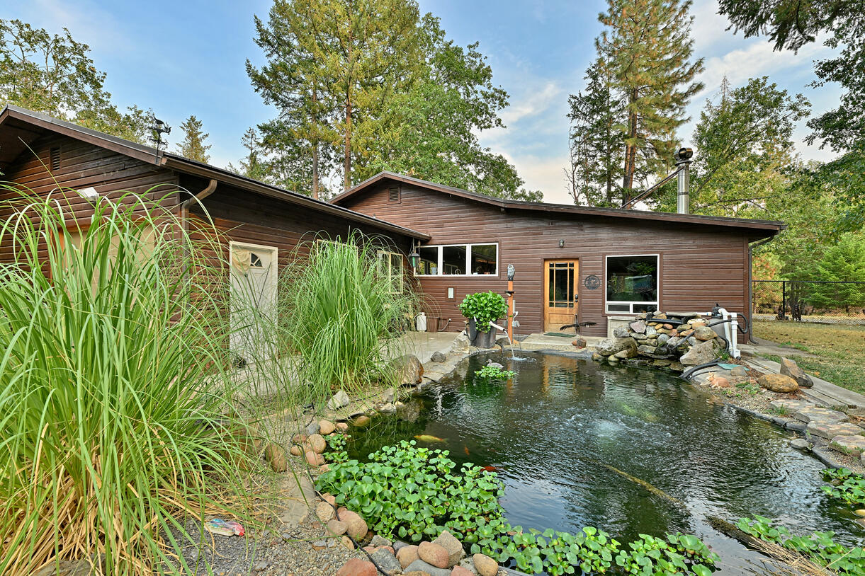 Incredible 19.61-acre wooded retreat featuring a spacious 1-bedroom, 2-bath, 2,208 sq ft home surrounded by nature. The open-concept layout offers abundant natural light and serene views through large windows. The kitchen boasts ample cabinetry and a generous walk-in pantry, while the living area centers around a cozy Toyotomi oil stove. The master suite includes a private bath with a large walk-in shower. A fully fenced 1-acre section is animal-ready—ideal for pets or a small hobby farm. Relax on the covered patio overlooking a tranquil koi pond and enjoy watching wildlife. The property is richly forested with fir, pine, black oak, and madrone trees, with private trails weaving throughout. Additional features include an attached garage, a large power-equipped shop, extra storage, and a 4-car canopy for all your toys and tools. Peaceful, private, and packed with potential—perfect as a hobby farm, retreat, or full-time residence.