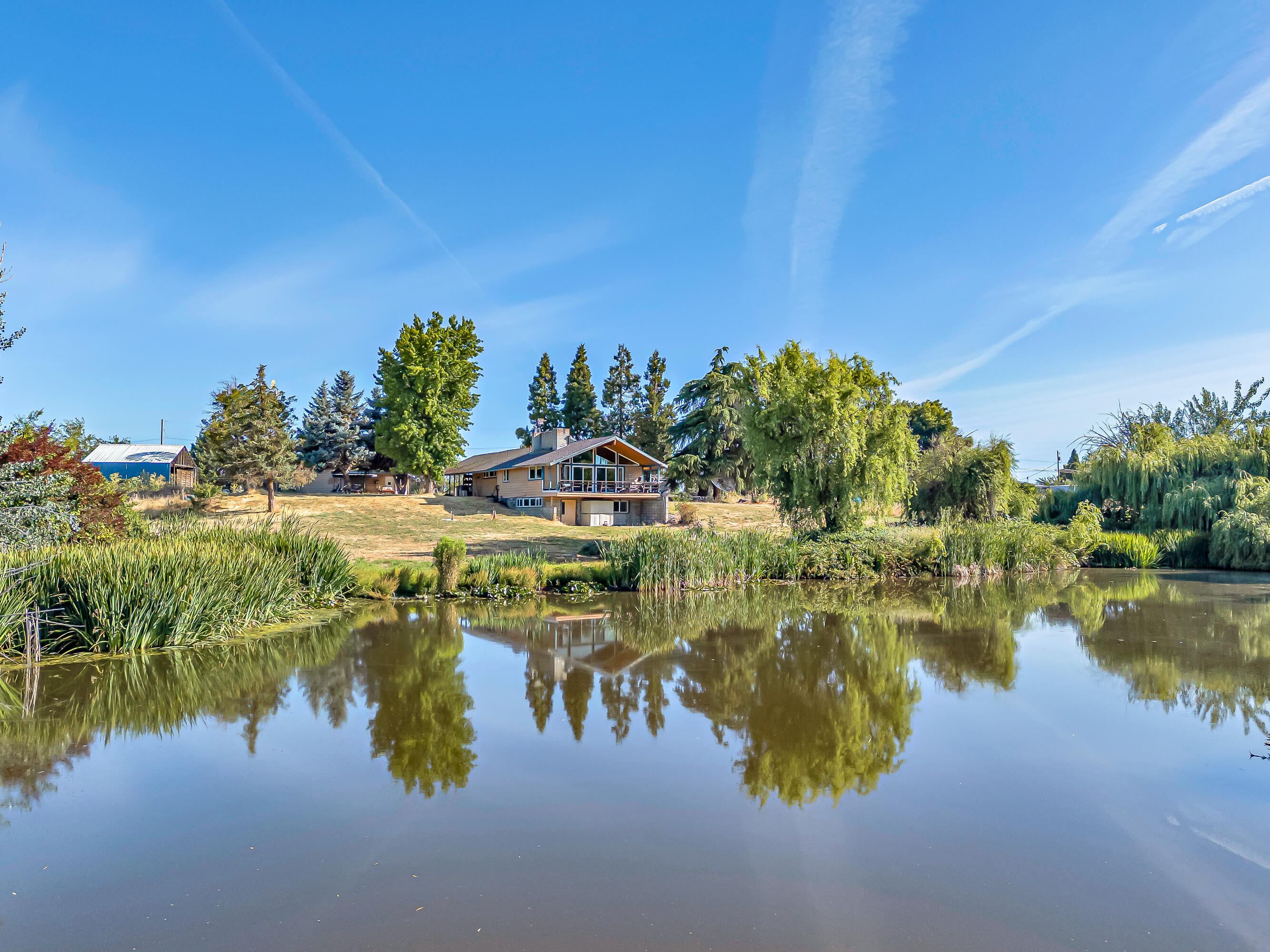 Extremely rare setting on a stunning year-round pond makes this a one-in-a-million property, truly unlike anything else. Lovingly owned by the seller for 43 years. Just minutes from town yet totally private, it features a gated entry, huge detached shop with concrete floors and power, large barn sits just behind the shop, flat usable grounds, high producing well (per seller), mature trees, and abundant wildlife. The home is fully vaulted with a floor-to-ceiling rock fireplace and natural light throughout. Main level has 2 bedrooms and a full bathroom. Downstairs includes a large 3rd bedroom, laundry area, and half bath. Includes city sewer and natural gas. Bright, open layout with tons of windows to enjoy the incredible views. Covered carport, full RV hookups, and just 4.3 miles to Fred Meyer. Ideal for animals or peaceful living. Rare opportunity with unmatched setting. Owner carry possible for qualified buyer.