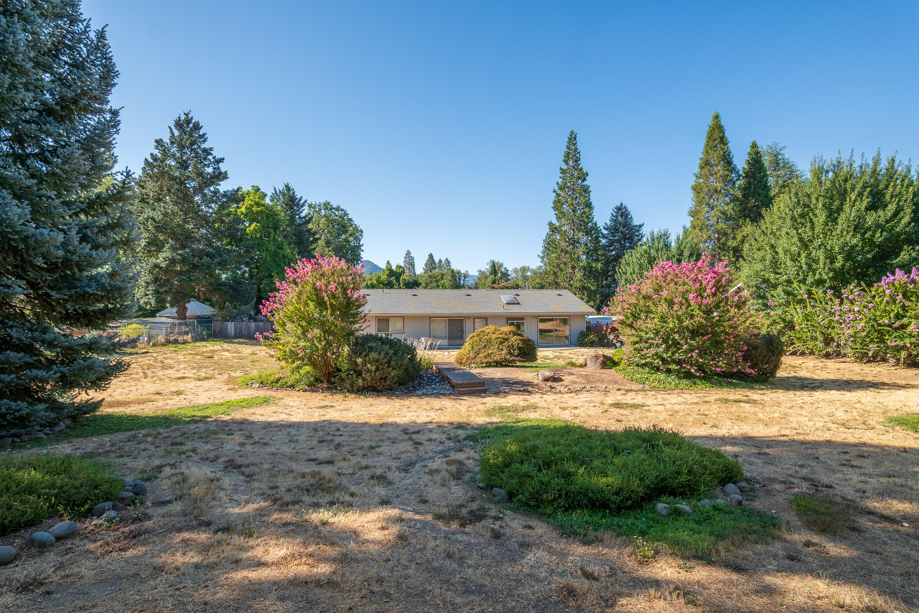 First time on the market! This inviting home greets you with a large front porch and French doors that open into a spacious living room with views of the expansive backyard. The thoughtful floorplan makes entertaining easy, featuring a galley kitchen with bar seating, a generous dining room, and direct access to the back patio. On the opposite side, you'll find 3 bedrooms and 2 bathrooms, creating both comfort and privacy. Set on a fully fenced and gated .85-acre lot within Grants Pass city limits, the property offers abundant parking, an additional 400 sq. ft. garage, and endless possibilities. Bring your vision—whether it's creating a private backyard retreat, adding an ADU for multigenerational living or rental income, or exploring subdivision potential (buyer to do due diligence). This home is ready for your ideas to shine and for its next chapter to begin!