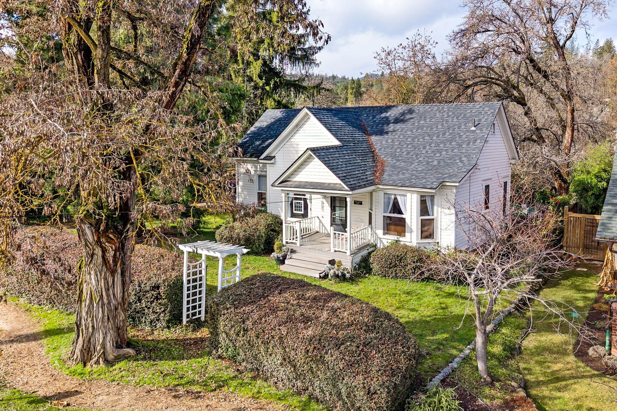 Built in 1872, the historic Ulrich House, is a charming single story home right in the heart of downtown Jacksonville. Lots of room for hobbies or outdoor entertaining with a 1/3 acre lot that features Daisy Creek along the rear property line. Detached guest qtrs (included in the main home sf) include a full bath & kitchenette, would make a great studio or office. 
The main house has an open living & dining rm w/ high ceilings & original fir flooring throughout most of the house. The galley kitchen has abundant natural light, a breakfast nook, & an area for a desk. It also has a large pantry. The primary has a built-in dresser & a walk-in closet.  There is also another bedroom w/ French doors, an office nook, & a full bathroom. A large laundry/mud room is off the kitchen & leads to the backyard. The yard is open & sunny, featuring a large patio, firepit, a gazebo w/ a hot tub, a storage shed, & room for gardening. Additional storage is located adjacent to the detached guest quarters