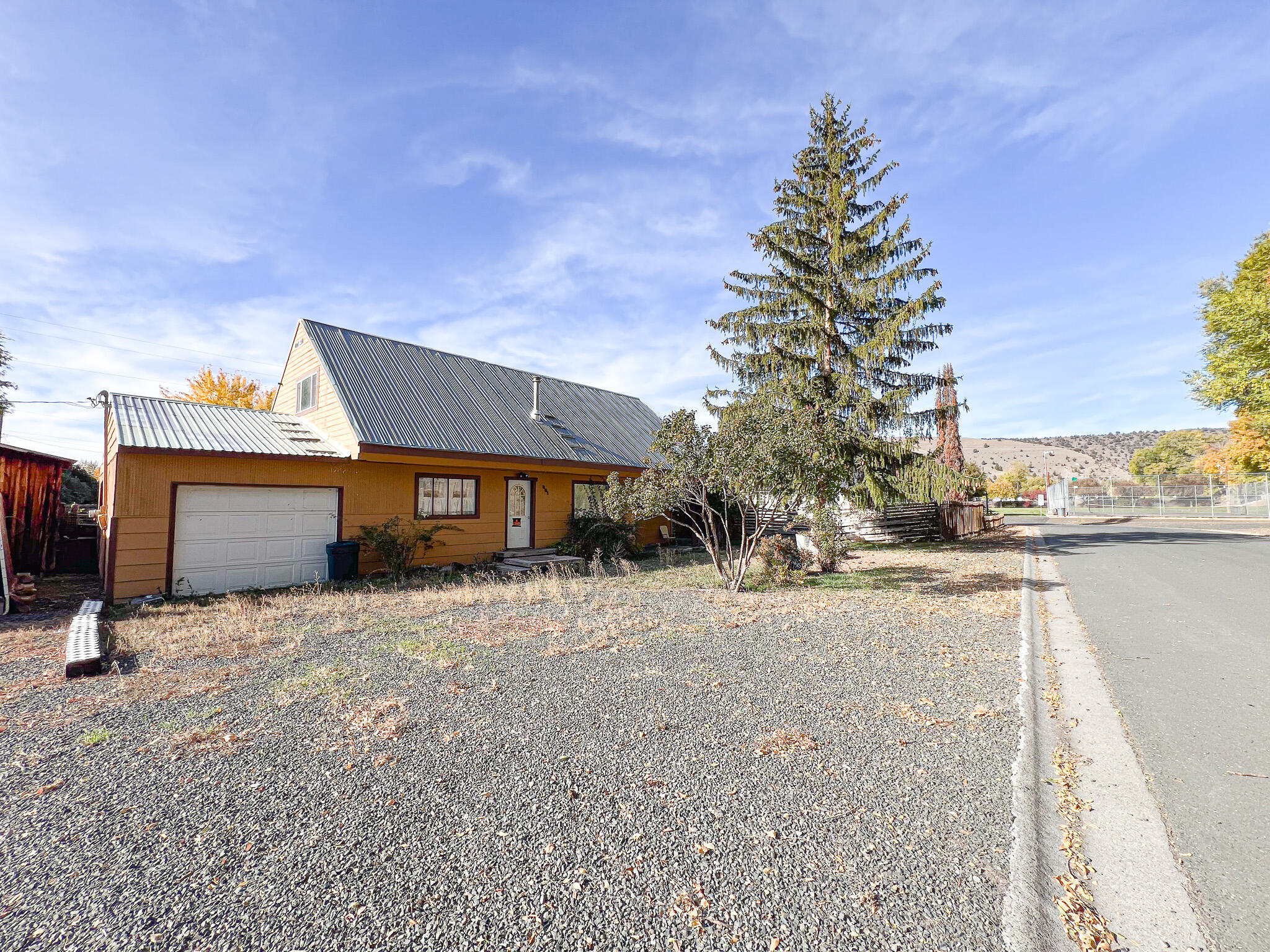 This 1950s home has undergone some remodeling.  It features vinyl windows and a tin roof. The flooring is a mix of laminate, wood, tile and carpet.

The homes heating is provided by a wood stove and an oil monitor stove. On the main level, there are two bedrooms, each with an armoire. The main level bathroom features a newly installed tub surround, vanity, and stylish tile flooring. There is also a finished bonus room, although it lacks a heat source. The upper level offers a 360-square-foot space that can serve as a primary bedroom. It includes a walk-in shower and an additional office area. 
The property includes an attached garage with a concrete floor, and there is a 13' x 11' storage area with a dirt floor. The outdoor space features a fenced back yard and a grape vine. The lot size is 0.17 acres and you can see the city park from your front yard.

This home is attractively priced for a quick sale, so do not hesitate to reach out for more information today!