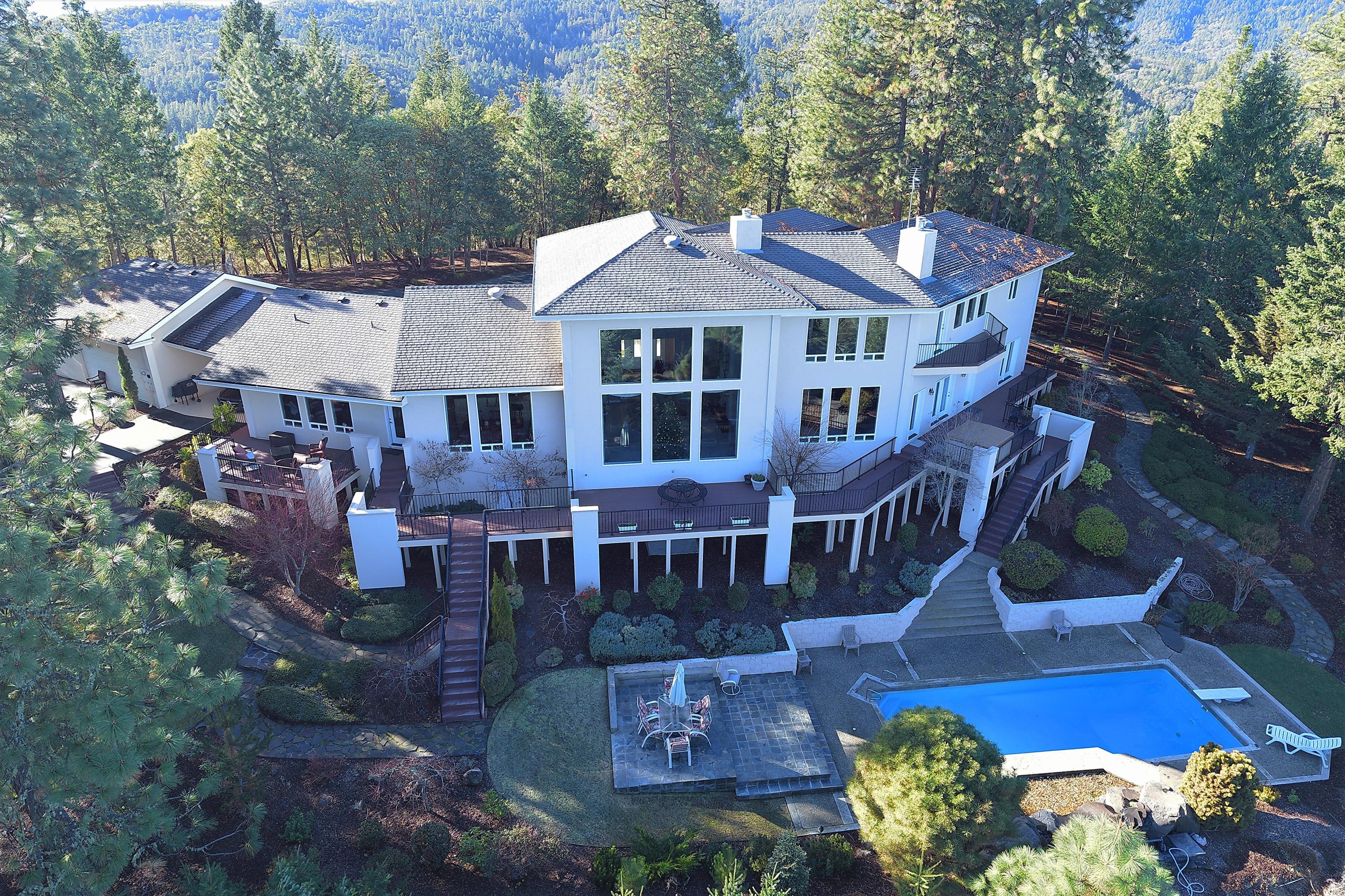 Southern Oregon living at it's finest!  Just two miles from historic Jacksonville, this elegant custom home on 20 forested acres offers unparalleled craftsmanship and exceptional amenities throughout. The private setting high atop Jacksonville Hill provides stunning panoramic views over the Rogue Valley & on to the Cascade mountain range, from almost every room. The grand front entry leads to a wide open floorplan featuring a spacious chef's kitchen with island & walk in pantry, great room, office, family room and two large guest bedrooms, each with  decks. The elegant master suite is sure to impress with private balcony, huge walk thru closet, gas fireplace and oversized jetted garden tub overlooking the city lights. There is also an oversized 3 car garage and a 970 ft. finished basement. Outside, the meticulously landscaped grounds are sure to impress, with a wrap around deck & hot tub overlooking the beautiful pool and patio w/water feature, perfect for summer entertainment.
