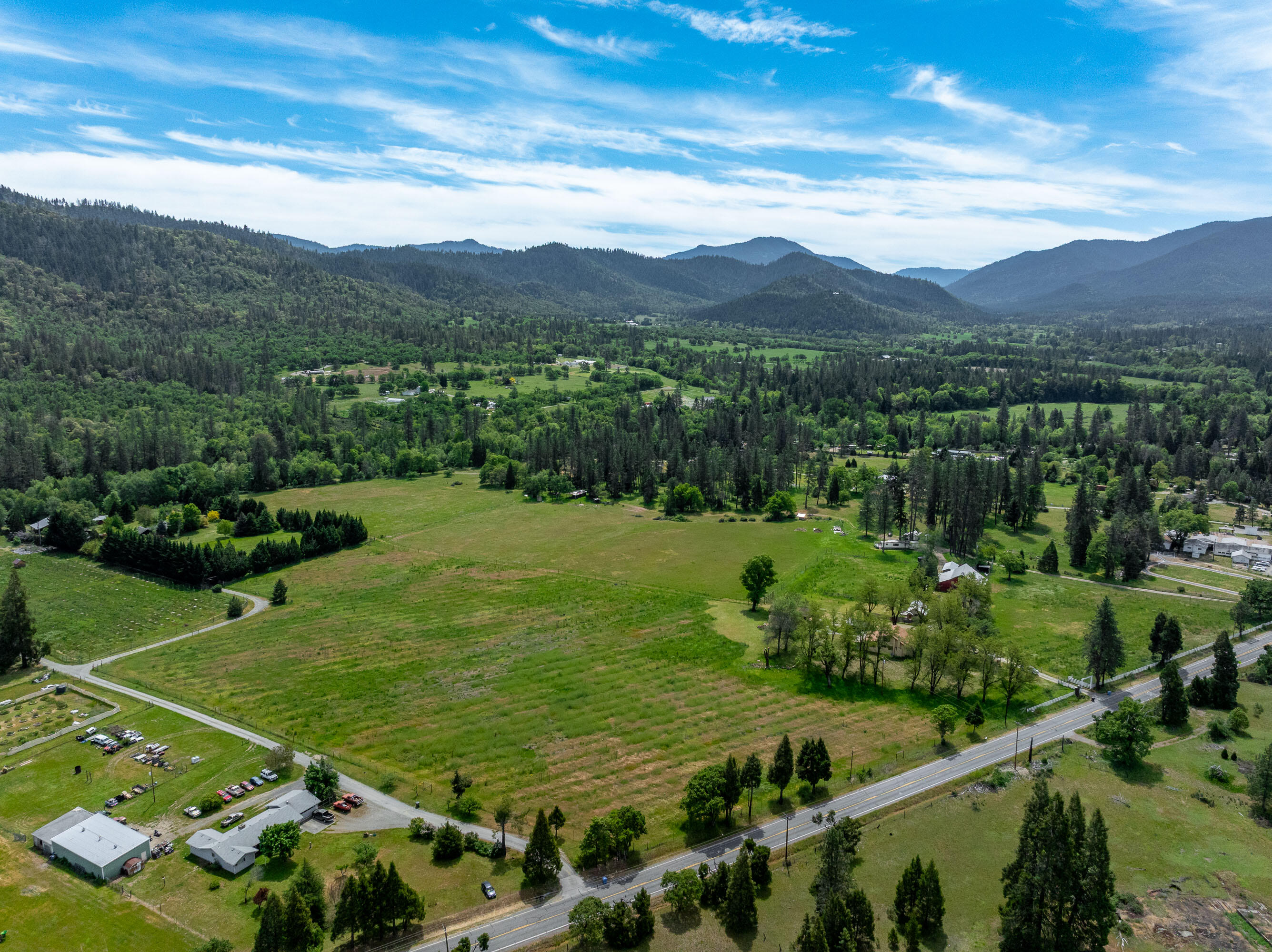 Amazing 81+ acre waterfront ranch in the heart of the Applegate Valley, offering exceptional versatility, income potential, and a premier location. This rare multi-family property includes 3 separate residences, each well-positioned for privacy and flexibility. With RR-5 zoning, the ranch carries significant development potential, creating incredible opportunities for expansion, family compound living, or long-term investment. The land is remarkably flat and usable, transitioning gently into beautiful sloped terrain, adjacent to BLM land. A historic barn, large shop, and extensive infrastructure improvements provide a powerful foundation for agricultural, livestock, or multi-use operations. The property boasts excellent irrigation water rights, a superb high-producing domestic well, and open pastures. Comprising four large parcels, the ranch is surrounded by gorgeous mountain views and offers unmatched tranquility while remaining close to everything—just 20 minutes to Grants Pass.
