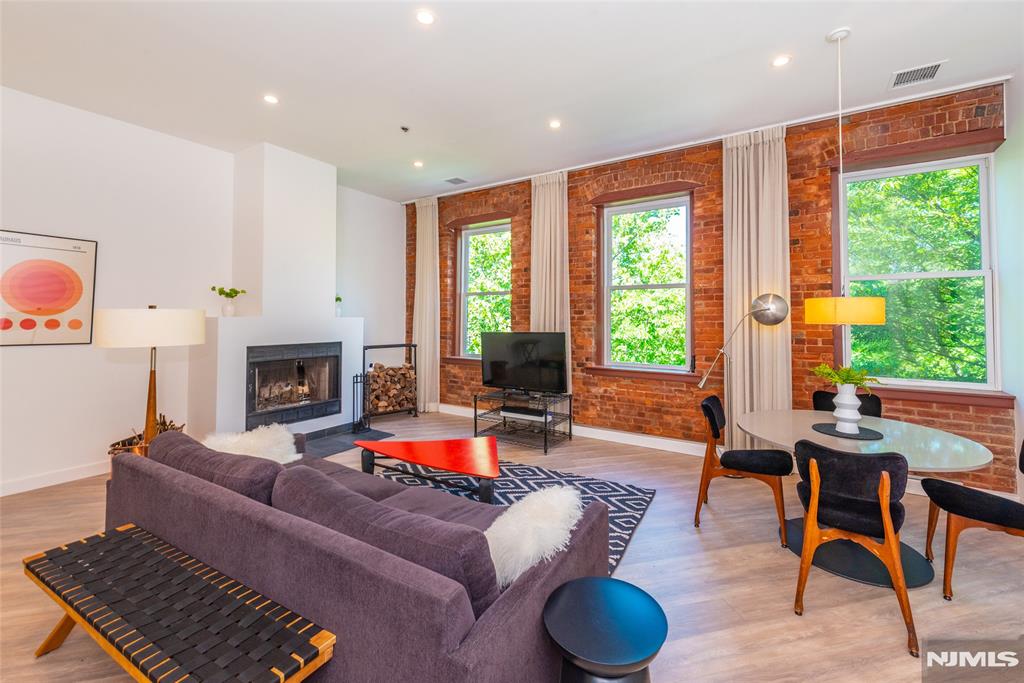 Set against the backdrop of the picturesque riverfront setting, this top-floor corner residence showcases one of The Mill's most architecturally distinctive residences. Three perfectly symmetrical oversized windows framed by exposed brick create a dramatic focal point in the main living area, highlighting the historic character that makes The Mill so sought after. The living room features a wood-burning fireplace that anchors the room, creating a unique setting. Extensively renovated, the residence offers approximately 1,156 square feet of updated living space. The kitchen features modern cabinetry, Quartz countertops, updated appliances, while both bathrooms have been renovated. All windows throughout the condo have been upgraded, enhancing efficiency. The primary suite is a standout feature, offering a rare arched picture window overlooking the river and greenery, a walk-in closet, and a private en-suite bath. The second bedroom is generously sized and serviced by a renovated hall bath. A dedicated utility and laundry room with full-sized washer and dryer provides functionality. Positioned on the top floor and benefiting from its corner location, the condo feels private with tranquil river views and treetop vistas. Residents of The Mill enjoy over 12 acres of maintained grounds and amenities, including a clubhouse, fitness center, tennis courts, swimming pool, and walking paths. The location is convenient to restaurants, shopping, major highways, and NYC transportation.