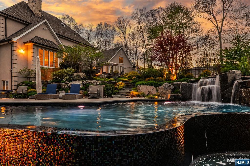 Welcome to Bear Rock Estates, where luxury, lifestyle, and location converge on 2.75 acres of lush, professionally landscaped grounds; an exceptional private retreat designed for elevated living and effortless entertaining. A grand two story foyer sets the tone, leading to a custom chef's kitchen with high end appliances, an expansive center island, a cozy breakfast nook, and a walk-in pantry. The kitchen flows seamlessly into the great room, anchored by a stunning double sided gas stone fireplace, and complemented by formal living and dining rooms, plus a private office. The first floor primary suite is a sanctuary, featuring a sitting area, spa like en suite bath, and a generous walk-in closet. Upstairs offers four beds three w walk-in closets two full baths, and a spacious finished playroom. The lower level is an entertainer's dream, complete with a custom wine cellar, wet bar, open concept home theater, private gym, full bath, and game room with walkout access to your own private oasis. Outdoors, indulge in a resort style backyard with multi level entertaining spaces, highlighted by a one of a kind infinity edge pool overlooking serene wooded views, an outdoor kitchen with a brick pizza oven, and a hot tub. Additionally, 3 car garage plus lift, radiant heated floors on the first level, Sonos audio throughout, and a new roof (2025). Ideally located near parks, hiking trails, top rated schools, fine dining, and convenient access to NYC via bus and Towaco Train Station.