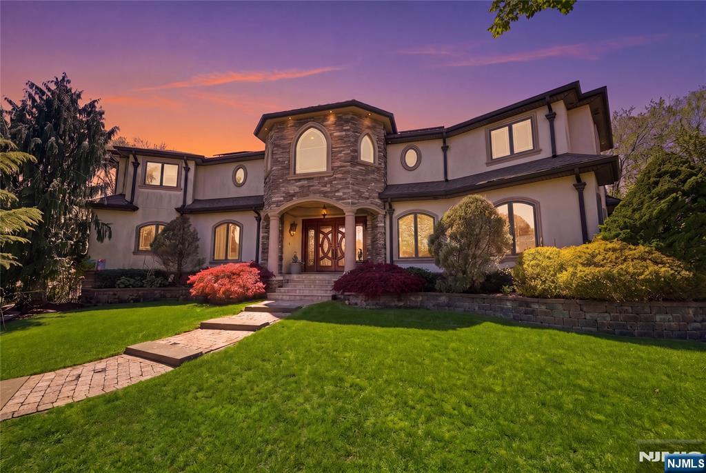 Experience elevated luxury living in this one-of-a-kind Paramus Colonial estate, where timeless elegance meets resort-style comfort. Offering 6 bedrooms, 5 full baths, 2 half baths, and approximately 10,800sq ft of impeccably designed living space, this grand residence sits on 2 beautifully maintained acres and showcases true craftsmanship throughout. A striking circular entry foyer welcomes you into a home featuring a full-house 3-story elevator, setting the tone for both sophistication and convenience. The main level is designed for upscale entertaining with an expansive great room and dual fireplace, formal living and dining rooms, a spacious family room, and a gourmet eat-in kitchen equipped with stainless steel appliances, along with a laundry room and dumbwaiter. Upstairs, generously sized BR each feature en-suite baths and walk-in closets, highlighted by a luxurious primary suite complete with a private sauna and whirlpool spa. The fully finished basement expands the living space with a salon room, private theatre room, additional BR, kitchen, and a large recreation area, perfect for entertaining, extended living, or multi-generational use. This exceptional property also features 3 attached garages plus 2 separate detached garage, offering ample space for vehicles & storage. Step outside to your own private resort-style backyard, with a stunning waterfall centerpiece and beautifully designed outdoor space, perfect for entertaining, relaxation, and year-round enjoyment.