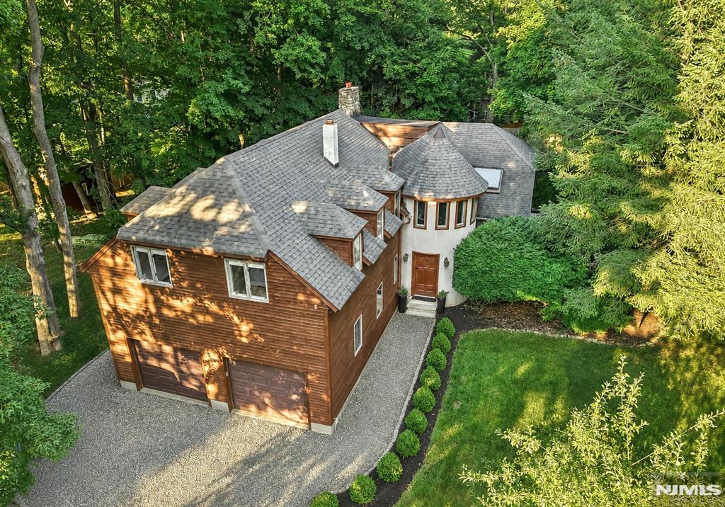 Set on approximately 0.75 acres of beautifully landscaped grounds in River Vale, this distinctive 4-bedroom, 2.5-bath home offers inviting spaces, architectural charm, and a wonderful connection to the outdoors. A formal entry foyer opens to a spacious kitchen that flows into a wraparound dining area overlooking the sunken family room, where a wood-burning fireplace and exposed stone wall create a warm and memorable focal point. A separate den with a beamed ceiling offers flexible space to relax, work, or gather, while two decks flank either side of the home - extending the living space outdoors. Upstairs, the spacious primary suite features a private bath and a unique turret-style sitting room enveloped in windows perfect as a home office or nursery. Three additional generously sized bedrooms and a full hallway bath complete the second level. Outside, professionally designed landscaping frames a private backyard ideal for entertaining, recreation, or quiet enjoyment. An attached two-car garage adds everyday convenience to this character-filled home set in top Bergen County school district.
