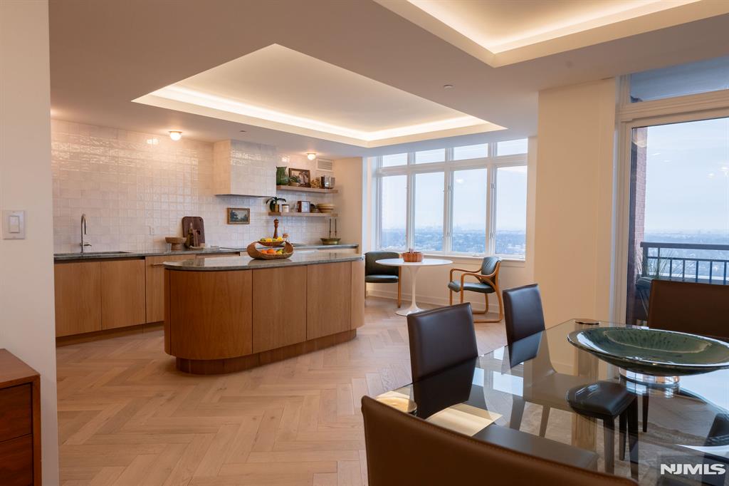 Perched at The Top, SOMA's premier luxury condominium, this fully renovated 3-bedroom residence showcases elevated design, exceptional craftsmanship, and sweeping NYC skyline views. Thoughtfully reimagined with a full designer renovation, every surface and finish has been curated with exceptional taste and attention to detail. An east-facing exposure fills the home with beautiful natural light throughout the day, enhanced by expansive windows and a seamless indoor-outdoor connection to a private balcony. New flooring laid in a sophisticated herringbone pattern, paired with sound-reducing underlayment, adds both style and comfort underfoot. Each of the three spacious bedrooms features its own ensuite full bath. The primary suite features a dressing area and bath with a soaking tub, stall shower w/new glass door, and refined new tile work. A stylish powder room off the hallway is ideal for guests, while custom built-in closets throughout provide exceptional storage solutions. The showstopping kitchen features custom wood cabinetry, marble counters, open shelving, and new appliances. A striking rounded center island anchors the space. Thoughtfully selected light fixtures and cove lighting on dimmers create the perfect ambiance throughout. Boasting one of the largest floorplans in The Top at 2500+ sqft, this home offers refined suburban living in the vibrant heart of Essex County, just moments from everything South Orange and Maplewood have to offer.