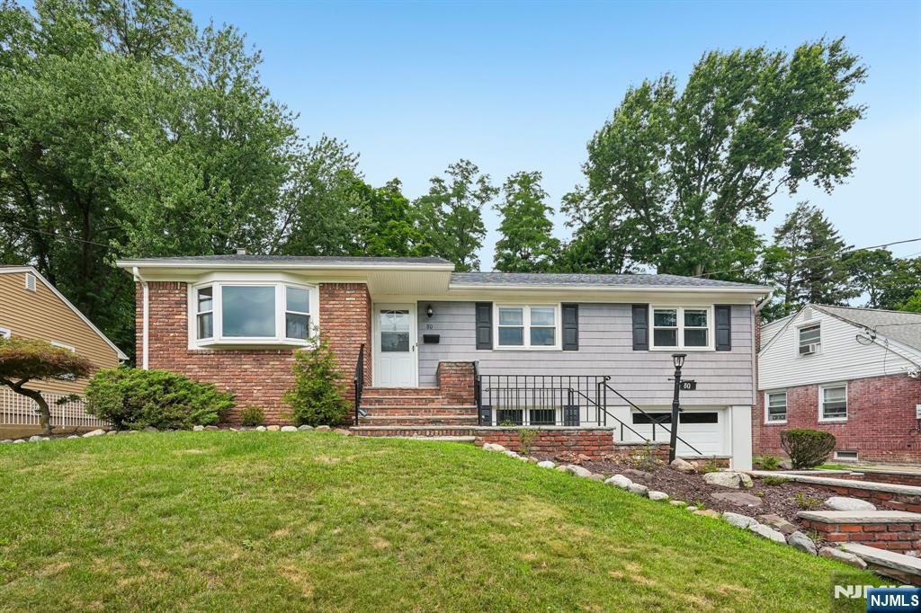 Welcome home to this well-maintained 5-bedroom, 2 full and 2 half bathroom Raised Ranch nestled on a manicured lot in the heart of Cedar Grove. A welcoming entry foyer leads into the spacious living room, where a large picture window fills the space with natural light and creates a warm, inviting atmosphere. The living room flows seamlessly into the elegant dining room, offering the perfect setting for everyday meals or entertaining guests. The adjoining eat-in kitchen features custom cabinetry, ample counter space, and a separate dining area. Just beyond, the cozy family room with a wood-burning stove provides the ideal place to gather on chilly evenings. The primary bedroom offers generous closet space and an en suite bath, while four additional bedrooms, a full bath, and a powder room provide flexibility for guests, or a home office. The finished lower level expands the living space with a second kitchen, dining area, laundry, a recreation room with a built-in bar and fireplace, plus a private office, powder room and workshop. Outside, the wooded backyard offers a peaceful setting with plenty of room for relaxing, entertaining, and outdoor activities. New roof and chimney. Complete with a 1-car attached garage, ample driveway parking, and a convenient location near NYC transportation, shopping, dining, parks, and schools, this home offers the perfect blend of space, comfort, and everyday convenience.
