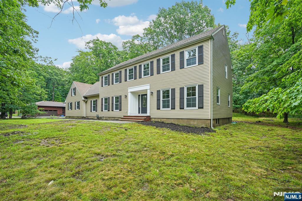 Welcome home to this beautifully updated 5-bedroom, 2.5-bath Colonial nestled on a well-manicured, private wooded lot. Step into the inviting entry foyer that opens to the expansive main living area. The spacious living room provides a bright, welcoming setting for everyday living and effortless entertaining, flowing seamlessly into the cozy family room with exposed wood beam ceilings and a classic brick fireplace, perfect for relaxing evenings or movie nights. The elegant dining room is ideal for intimate dinners or larger gatherings and connects to the eat-in kitchen featuring custom cabinetry, quartz countertops, a stylish backsplash, stainless steel appliances, and a separate dining area. Sliding glass doors fill the space with natural light and lead to the rear patio. A first-floor bedroom, mudroom, and powder room add flexibility and convenience. Upstairs, the primary suite offers a large closet and private en suite, while three additional generous bedrooms and a full bath provide plenty of room for versatile living. The full unfinished basement offers abundant storage, laundry, utilities, and endless potential for future living space. Step outside to the patio, perfect for grilling, outdoor dining, and entertaining, overlooking the expansive wooded backyard with room to play, unwind, and enjoy nature. A 2-car attached garage and ample driveway parking complete this exceptional home, conveniently located near NYC transportation, shopping, and dining.