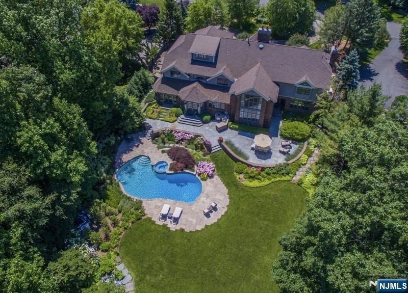 Live like you are on vacation every day in this modern North Caldwell estate, where bold design meets resort-style luxury. A dramatic marble entry and sweeping staircase set the tone, complemented by soaring ceilings, sleek millwork, and wide plank hardwood floors. Built with steel beam construction and surrounded by lush landscaping, water features, and curated gardens, the home offers exceptional privacy and tranquility. The Canterbury-style chefâ€™s kitchen anchors the main level with high-end appliances and timeless finishes, opening to a sun-filled glass solarium, perfect for year-round living. Upstairs, the primary suite delivers a true retreat with a spa bath, oversized shower, and soaking tub, while all additional bedrooms are spacious and ensuite.The finished lower level transforms the home into a private club, featuring a mahogany bar, climate-controlled wine cellar, FULL SWING GOLF PRO simulator, fitness room, projection theater, and lounge spaces designed for entertaining.
