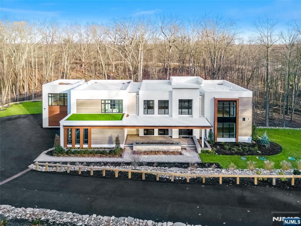 This striking two-story contemporary home greets you with a dramatic foyer featuring rich wood paneling, a sculptural lighting fixture, and a custom staircase with custom glass railings that set the tone for the elegant design throughout. The spacious Great Room, centered around a custom fireplace, flows seamlessly into a sleek, state-of-the-art kitchen with brand-new stainless-steel appliances. Large sliding doors lead to a generous patio with a second fireplace, perfect for refined indoor-outdoor entertainment. The main level also includes a stylish powder room, a versatile bonus room, a well-appointed mudroom, and access to both a two-car garage and a separate one-car garage for added convenience. Upstairs, the bedrooms include the impressive Primary Suite with a walk-in closet and a spa-like en suite bath. Oversized windows and soaring ceilings throughout flood each room with natural light, enhancing the homeâ€™s open, airy feel. Set back from the street on a large lot, the home is accessed by a long, elegant driveway and exudes a refined yet welcoming presence. The owner has put in green-grade sod to complete the exterior. 10 Big Ramapo offers everything you need: poured concrete foundation, steel siding, butcher block stairs, custom glass railings, decorative wall accents, and top-tier plantings. This is contemporary living with a distinctly elevated perspective. Come see it for yourself!