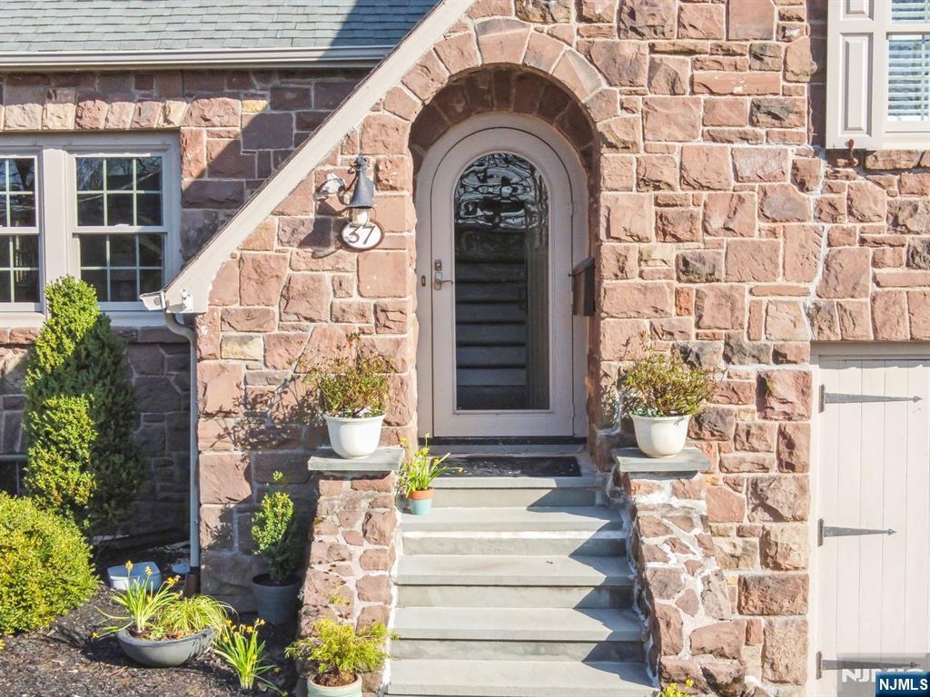 Just over the hill from Montclair & near restaurants, shopping, & NYC transport, this enchanting stone Tudor sits on a picturesque cul-de-sac. Every corner invites you to settle in & stay. A stunning living room boasts cathedral ceilings, leaded glass windows, & a grand stone wood-burning fireplace. Pass through a charming sitting room (perfect as a bar or reading nook) into the light-filled family room with another fireplace & sliding doors to your private oasis. The elegant dining room offers garden views, while the sunlit breakfast room & patio provide a serene start to the day. A mud/laundry room off the garage keeps life organized. Upstairs, find three spacious corner bedrooms, including a serene primary ensuite & a stylish hall bath. The lower-level rec room features a cozy gas fireplace, perfect for unwinding. A lush, private backyard backs up to a wooded area, creating a true retreat. With timeless charm & modern comforts, this home is both sophisticated & welcoming.