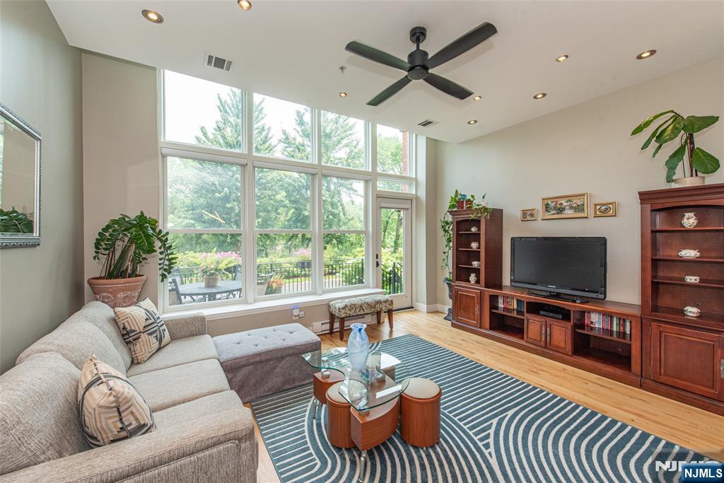 First floor living with a private outdoor space is a combination that's hard to find at The Mill. This beautifully updated condo features its own deck overlooking the landscaped grounds, with direct access to the community's walking paths right from your door. Inside, soaring ceilings and dramatic floor to ceiling windows fill the space with natural light, while hardwood floors, recessed lighting, custom blinds, and a thoughtfully designed layout create an open, inviting feel. This is one of the only one bedrooms units that offer a bonus half bath. The renovated kitchen showcases quartz countertops, a full height quartz backsplash, two tone cabinetry, stainless steel appliances, and generous prep space. The spacious primary suite offers oversized windows with peaceful views of the grounds, while updated bathrooms and abundant storage add everyday comfort. Residents enjoy a swimming pool, fitness center, tennis courts, walking and jogging paths, and beautifully maintained grounds. The train station is just one block away, a bus stop is across the street, and major highways are only minutes away, making commuting simple. With its rare first floor location, private outdoor space, and exceptional setting, this condo offers a lifestyle few residences at The Mill can match.