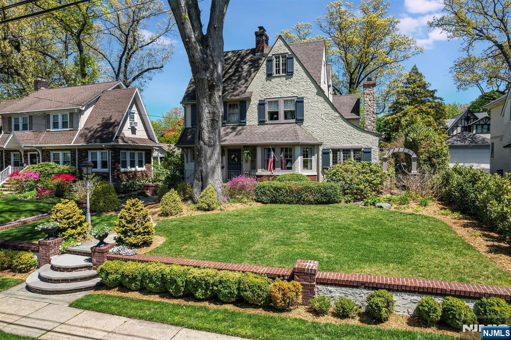 Welcome home to this gorgeous Tudor Colonial, perfectly situated on a charming street just steps from the elementary school, town center, and NYC train and bus. Thoughtfully updated and expanded over the years, this sun filled home offers generous living spaces and exceptional flexibility for modern living. The main level features an entry foyer with updated powder room, a relaxing formal living room with fireplace opening to the bright library. Large dining room area off the kitchen and French doors leading to an inviting family room addition with a second fireplace and convenient rear mudroom. The beautifully updated kitchen includes quartz countertop & marble top table, updated appliances and a spacious separate breakfast room. The second level offers a large primary suite with walk in closet, custom bath with steam shower, a second bedroom with en-suite bath, a third bedroom and a hall bath. The upper level includes two additional bedrooms, a hall bath, and a private office. The finished lower level provides great bonus space with a gym, office, living room & powder room. The oversized, rebuilt and expanded two car garage includes water, electric, loft area & heat. Additional amenities; beautiful moldings throughout, radiant heat in the LR & primary bath, wet bar in FR, fish pond with water feature, outdoor fireplace & bluestone patio, FR FPLC with Delft tile surround. A lovely restored home in an unbeatable location, ready to welcome its next owner.