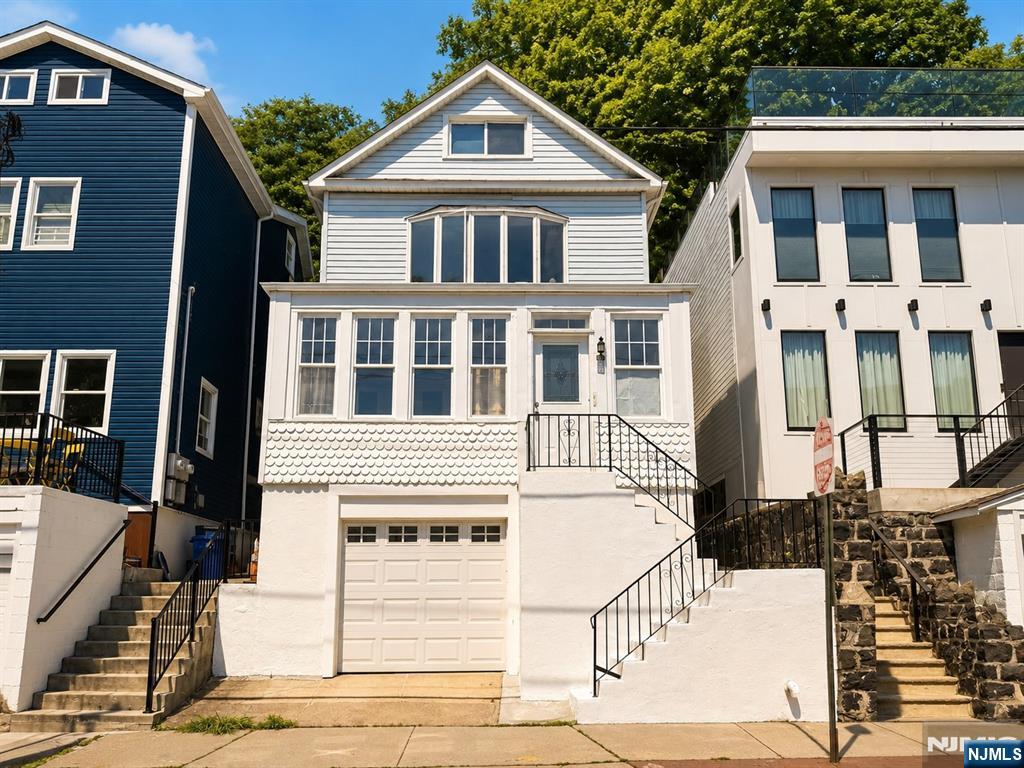 Bright and inviting, this 4-bedroom, 2-bath home offers the perfect combination of space, functionality, and an unbeatable location just moments from NYC. Filled with beautiful natural light, the home features an open-plan kitchen, living, and dining area designed for effortless entertaining, along with a charming sunroom and a versatile bonus room ideal for a home office, gym, playroom, or potential 5th bedroom. The private backyard patio is perfect for relaxing or hosting guests, complete with custom built-in bench seating. Additional highlights include a 1-car garage and generous basement storage, providing valuable extra space rarely found this close to Manhattan. Situated on a sleepy, low-traffic intersection of one-way streets, the home offers a peaceful neighborhood feel while still enjoying beautiful views of the city. Enjoy exceptional convenience with the NYC ferry just 3 blocks away and NYC buses only 2 blocks from your door. Whole Foods, Pilates studios, cafés, restaurants, and everyday essentials are all just a short stroll away, creating an effortless walkable lifestyle minutes from Manhattan. A rare opportunity to enjoy sunlight, outdoor living, storage, parking, and seamless NYC access all in one exceptional home.