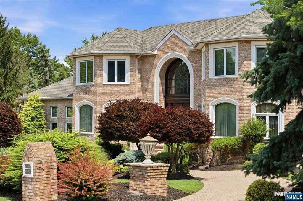 A grand brick residence with resort-style grounds, this home makes an unforgettable first impression with manicured landscaping, a circular paver approach and a dramatic arched entry. Inside, a two-story foyer sets the tone with stone floors, a sweeping staircase, wrought-iron details, custom millwork and a striking light fixture. Elegant formal spaces unfold from the entry, including a soaring living room with columned detail, an expansive dining room and a richly finished office with built-ins. The kitchen is designed for scale, with custom cabinetry, stone counters, premium appliances, a large island, extensive storage and a generous breakfast area wrapped in windows. Nearby, the family room offers warm wood floors, a fireplace, impressive ceiling height and direct access to the outdoor living spaces. The main level also includes a private bedroom suite, ideal for guests or extended stays. Upstairs, a gracious landing overlooks the foyer and leads to multiple bedroom suites, including a substantial primary retreat with a sitting area, large walk-in closet and spa-like bath with soaking tub, dual vanities and oversized shower. The lower level expands the home with a recreation room, billiards area, bar, secondary kitchen, bedroom, full bath and abundant storage. Outdoors, mature trees and layered plantings create a private setting with manicured lawns, a large terrace, outdoor kitchen, pool, spa and rock waterfall. A rare blend of presence, scale and everyday resort living.