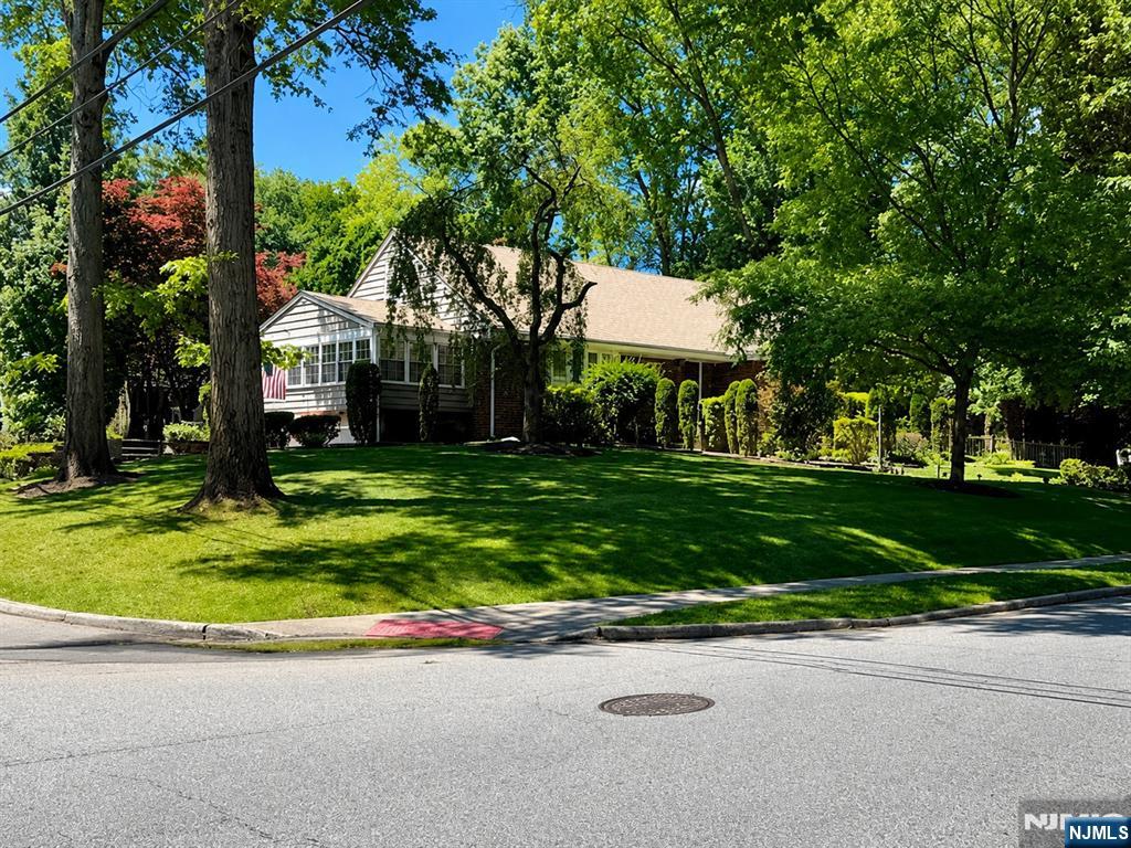 Set on an expansive 94 x 151 foot corner lot directly across from Roosevelt Common, this thoughtfully expanded Tenafly home offers a rare combination of space, setting, flexibility, and long-term value. With mature landscaping, multiple living areas, a finished lower level, and meaningful updates throughout, this is an opportunity to own a substantial, well-cared-for home in one of Bergen County's most sought-after communities. Offering approximately 2,458 sq ft of living space, the home features 3 bedrooms plus a versatile den, 3 full bathrooms, 1 half bathroom, hardwood floors, a wood-burning fireplace, an attached garage, and a bright enclosed sunroom overlooking the property's mature greenery. The finished lower level provides excellent flexibility for recreation, work-from-home needs, guests, hobbies, or storage. Over the years, the home has been thoughtfully improved with renovated bathrooms, updated mechanical systems, a newer roof in 2023, and attractive paver driveway and walkway enhancements. The oversized corner property is framed by mature trees, established gardens, and generous lawn space, creating a private and picturesque setting rarely found at this price point. Ideally located near schools, shopping and dining, Roosevelt Common, and approximately 1 minute from NJ Transit 166 Express bus service to Midtown Manhattan/Port Authority, this home offers space, comfort, outdoor presence, and long-term potential in a highly desirable Tenafly location