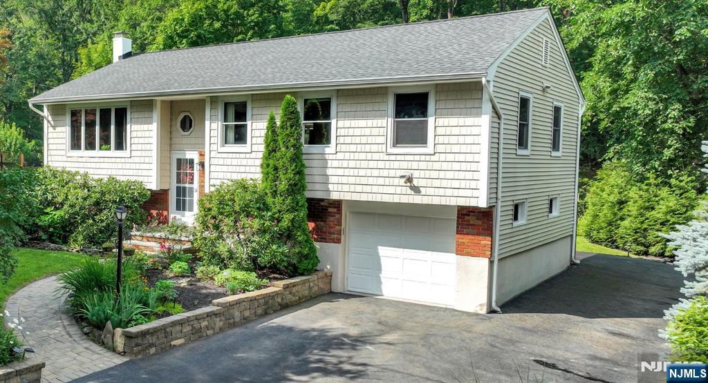 A backyard sanctuary like no other in lower West Milford with quick and convenient access! Updated home nestled in nature, surrounded by mature lush trees, natural hardscape, garden bridge over tranquil stream in distant rear of yard. Garden deck. Natural gas. Wood floors. Newer: roof w/ice guards, central air, hot water baseboard heating, Pella windows, well pump and holding tank, 200 amp electrical service. Kitchen with quartz counter, breakfast bar, stainless steel appliances. Living room with bay window open to dining room with French doors to 3 season room overlooking beautiful backyard with access to deck. Great lower level with extended living space, complete with summer kitchen, bedroom/office, full bath and family room with direct access to covered patio, hot tub and fire pit. Shed, dog fence, alarm system, generator hook-up. Minutes to shopping, restaurants, schools and town center.