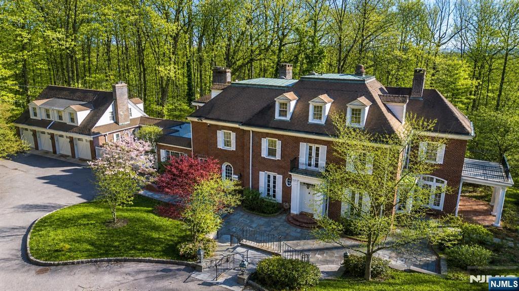 Set within the storied gates of Llewellyn Park, 5 Rocky Way offers a rare blend of privacy, scale, and timeless elegance on a wooded, secluded lot with a quiet, serene setting. A four-car attached garage with carriage house above provides exceptional flexibility, featuring a one-bedroom, one-bath residence with kitchen and living space ideal for guests, or creative use. The main home is designed for both grand entertaining and everyday comfort, showcasing a spacious eat-in kitchen with breakfast area ready for your personal vision, formal dining room, solarium, sun-filled living and family rooms, and a convenient first-floor powder room and laundry. Custom built-ins, five fireplaces, and beautiful hardwood floors throughout add warmth and character. A sweeping center-hall staircase leads to a gracious second level with 2 lovely primary suites, three additional bedrooms, and two baths. The third floor offers two more bedrooms, a full bath, and abundant storage. Outdoor living is equally inviting, with a private patio, covered patio, multiple balconies, and charming architectural details that enhance the home's classic character. Ample parking and easy access to major highways, NYC transit, and Montclair's shopping and dining complete this exceptional offering an estate-style retreat moments from everything