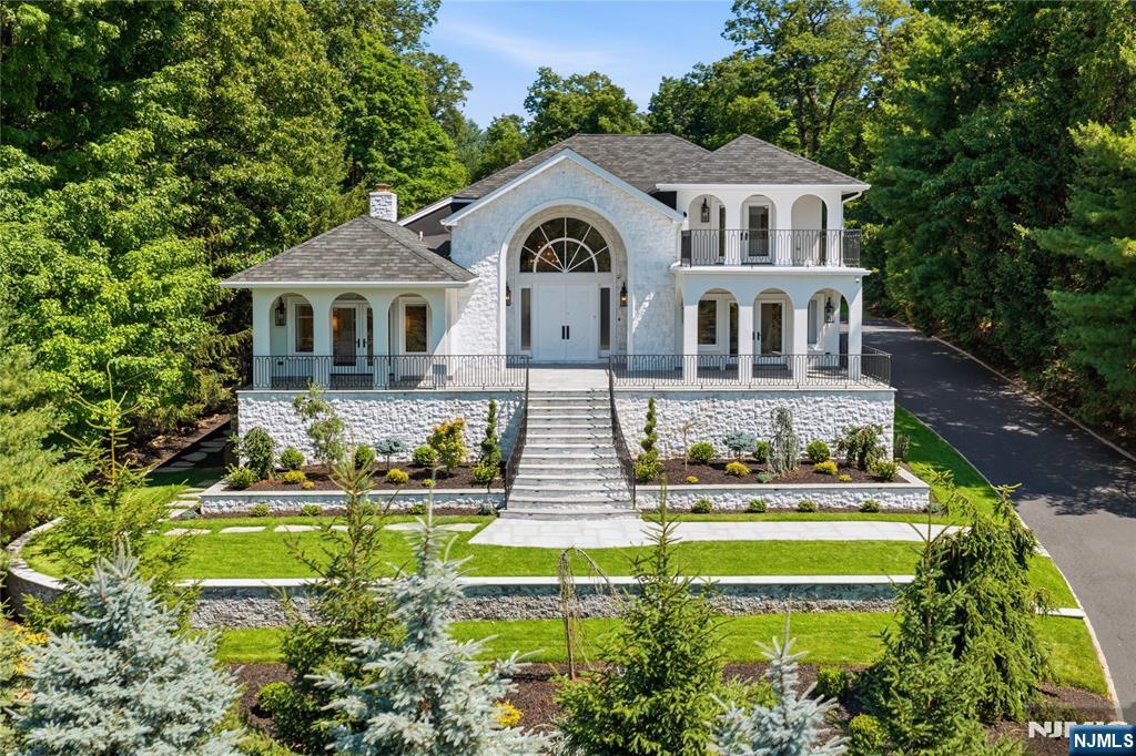 Arrive to a home that feels both luxurious and inviting, wrapped in mature greenery and introduced by a white stone-and-stucco facade, arched porticos, balconies and tailored ironwork. The story begins with a soaring foyer, where crystal chandeliers, paneled walls, wide-plank oak floors and a graceful curved staircase create a memorable first impression. From there, sunlight pulls you into elegant living and dining spaces, with arched windows, detailed millwork and a stunning fireplace adding warmth. The kitchen continues the sense of occasion: custom cabinetry, stone counters, a generous island, pendants, premium stainless appliances, a custom range hood and a breakfast area surrounded by nature. Two bedrooms on the first floor offer flexibility for guests or work. Upstairs, the primary suite is a private retreat with vaulted ceilings, a sitting area, balcony access, generous closets and a serene bath with soaking tub, skylight, floating vanities and a dramatic glass shower. Additional bedrooms are bright and thoughtfully placed, including one with balcony access. Downstairs, the finished lower level shifts the mood to leisure and entertainment, with a full bar, recreation lounge, billiards, games, fitness space, second kitchen, office, bath and storage. Outside, stone terraces invite dining, lounging and long afternoons by an outdoor fireplace, while open lawns and privacy plantings create a peaceful backdrop. A three-car garage completes the home. BOH, 7.2, 10-12.