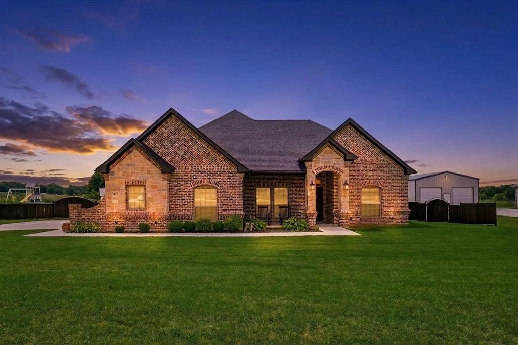 This single-story brick home opens to a bright interior with gorgeous wood-look flooring, recessed lighting, and an open-concept layout connecting the main living spaces. The living area features a floor-to-ceiling stone fireplace, large windows overlooking the backyard, and easy flow into the kitchen and dining areas. The kitchen includes dark wood cabinetry, granite countertops, stainless steel appliances, pendant lighting, and a large center island with seating. Rustic accents and open sightlines create a warm, functional space for everyday living and entertaining. The primary bedroom offers generous space, a tray ceiling, and a broad bay window that brings in natural light. The en suite bath includes a double vanity, a soaking tub, a glass & tile shower with rainhead & sprayer, and a vast closet with utility room access. Additional bedrooms are well-sized and include ceiling fans, ample windows, and convenient access to nearby bathrooms. Step outside to a covered back patio with wood accents, ceiling fan, TV mount, and plenty of room for outdoor seating and dining. The backyard features expansive green space, a fire pit area, and playground equipment, all set against open views of the surrounding landscape.  Nearby access to Hwys 199 and 114.  Just minutes from magnificent Eagle Mountain Lake with boating, fishing, trails, and more