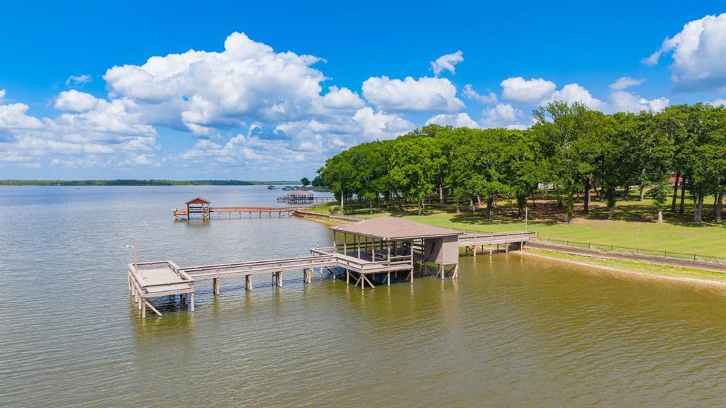 There are homes that impress, and then there are homes that quietly redefine what you thought was possible. This waterfront estate falls into the latter, where design, scale, and setting come together to create something that feels less like a residence and more like a private retreat shaped by intention. Life on the water carries its own rhythm, with the lake shifting in color from sunrise to dusk, bringing a sense of calm to everyday moments. Whether on the expansive deck with morning coffee or relaxing indoors, the view becomes part of how you live. With more than 280 feet of shoreline, over 4,000 square feet of living space, and 1,300 square feet of decking, the home is designed to embrace its surroundings. The boathouse, just over 1,500 square feet, includes a single slip with electric hoist, storage, a spacious party deck with a lazy swing, and a fishing platform for long afternoons by the water. A nearly 900 square foot garage offers ample space for vehicles and equipment. Inside, the kitchen opens seamlessly into the main living area, featuring granite countertops, stainless appliances, a beverage cooler, abundant cabinetry, and a large pantry, making it ideal for both entertaining and everyday living. The formal living room showcases a wood-burning fireplace, crown molding, and built-ins, while the dining room offers an elegant space with water views. A second living area with a cathedral ceiling and expansive windows captures sweeping lake views and serves as a natural gathering space. The primary suite provides a private retreat with a sitting area, lake views, and a well-appointed bath with jetted tub, dual vanities, walk-in shower, and large closet. Three additional bedrooms are generously sized, and a private office offers flexibility as a fifth bedroom. With multiple living spaces that invite you to unwind, entertain, or simply take in the stillness of the outdoors, this home offers privacy, presence, and a daily connection to something rare.