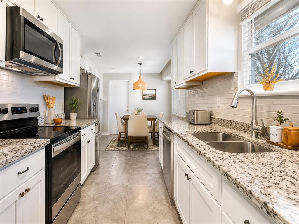 Assumable FHA Loan at 4.99%! Only 25 years left on this mortgage, total payment approximately $2,300! Located in desirable Buckner Terrace, minutes from Downtown Dallas and White Rock Lake, this thoughtfully updated home offers a comfortable, flexible layout with meaningful upgrades throughout. The beautifully renovated kitchen features white shaker ceiling height cabinetry, slab granite countertops, subway tile backsplash, and stainless steel appliances along with replaced ceramic tile flooring. Formal living and dining spaces provide excellent entertaining areas and feature a large bay window preserved during the remodel, bringing in abundant natural light. A cased opening connects the living and dining areas to the den - offering a more functional alternative to overly open floor plans. The den showcases a beamed ceiling, wood-burning fireplace, and built-in bookshelves and cabinetry, creating a warm, inviting gathering space. The spacious primary suite includes a walk-in closet plus a second closet, and an updated bath with a tub, granite-topped vanity, dressing area with granite countertop, and attractive tile flooring. Two guest bedrooms - one notably large - share an updated hall bath with a granite vanity, raised bowl sink, and replaced tile flooring. Luxury vinyl plank flooring runs through the living areas and hallway for durability and ease of maintenance. Major system and efficiency upgrades include all new Pella windows throughout (including sliding patio doors –$20K), replaced attic insulation, updated electrical service with a new panel, new gutters and a new patio covering designed to maximize natural light. The covered patio overlooks a large, fenced backyard with mature trees and a storage building, offering space to relax, garden, or entertain. A two-car rear-entry garage provides ample parking & storage. A well-balanced home that blends classic character, smart updates- ideally located in one of East Dallas’s most established areas