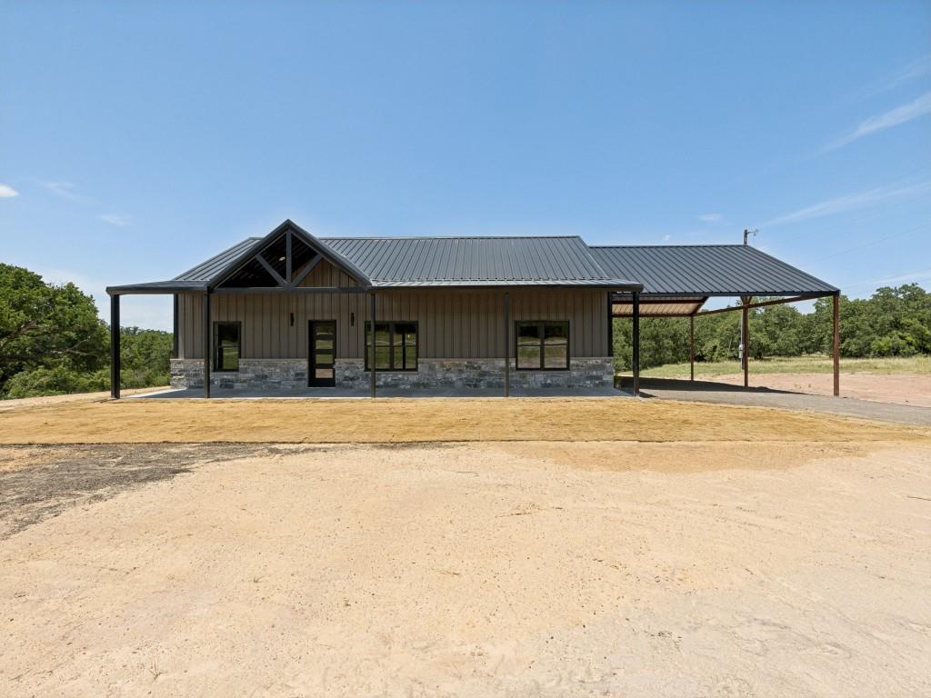Welcome to this exceptional luxury barndominium. Sitting on just over 3 heavily treed acres  Thoughtfully designed with high-end finishes and superior craftsmanship, this stunning home was built to impress. Constructed with durable red iron framing, it offers, sophisticated black grey exterior and inviting full-length front porch overlooking incredible views. Inside, you'll find an open-concept floor plan with soaring vaulted ceilings, expansive picture windows that flood the home with natural light, and a desirable split-bedroom layout designed for both comfort and privacy. Every detail has been carefully selected to create a warm yet refined atmosphere. The kitchen is truly the heart of the home, featuring gorgeous Level 7 granite, black stainless steel appliances, a gas cooktop, and custom live-edge dark walnut shelving that adds the perfect touch of rustic character while complementing the home's modern design.The luxurious primary suite offers a peaceful retreat with hand-scraped beams that continue into the spa-inspired ensuite bath. Imported Spanish tile and an elegant tumbled marble walk-in shower. Quality craftsmanship and designer finishes continue throughout the home, making every room as beautiful as it is functional.Step outside and enjoy the serenity of the oversized front porch, where you can relax with your morning coffee or unwind in the evenings while taking in the picturesque views and surrounding mature trees. The premium drought-tolerant sod creates a lush, thick lawn while requiring less water, offering both beauty and efficiency.The spacious 25' x 32' covered carport provides excellent versatility and can easily be enclosed to create a garage, workshop, or additional storage space to fit your needs.Conveniently located with easy access to the Metroplex, this property offers the perfect balance of peaceful country living and everyday convenience. This is more than just a home—it's a lifestyle you'll be proud to call your own.