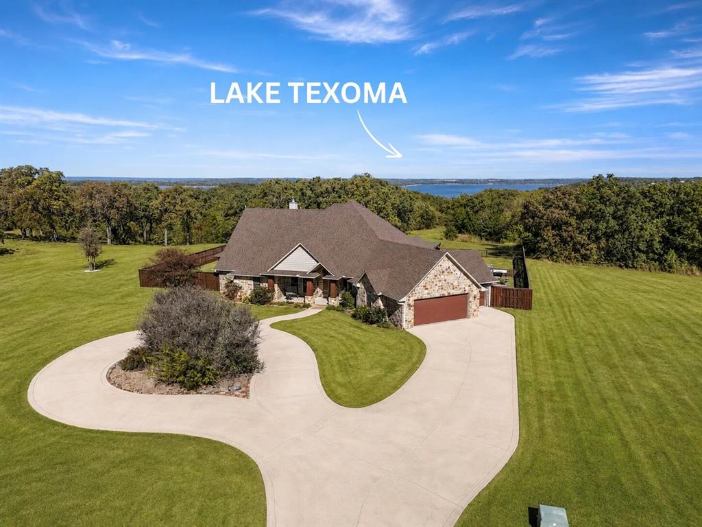 Welcome to this impressive custom home in the gated Texoma Bluffs community of Gordonville, set on 2.18 acres overlooking Lake Texoma and adjoining Corps of Engineers land. This is the rare combination of privacy, acreage, and lake lifestyle just minutes from the marina and over 14 miles of hike-and-bike trails along the Cross Timbers Trail.
Inside, soaring vaulted ceilings and a wall of windows fill the living room with natural light and lake views, all anchored by a floor-to-ceiling stone fireplace. The gourmet kitchen is built for real cooking and gathering: granite counters, walnut cabinetry, an expansive island breakfast bar, and a working pantry with its own prep counter and sink.
The primary suite captures sweeping lake views and offers a spacious bath and well-designed walk-in closet that doubles as a safe room, a thoughtful touch you won't find in most homes at this price point. A flexible bonus room off the living area works as a craft room, or storage room with a convenient half-bath just steps from the backyard.
Outside, a covered patio and sunroom create comfortable space for relaxing or entertaining in any season, while thoughtful landscaping enhances privacy and complements the natural setting. Built in 2011, the home features energy-efficient spray foam insulation and modern finishes throughout.
Minutes to the lake, the marina, and miles of trails this is acreage living without giving up convenience.
