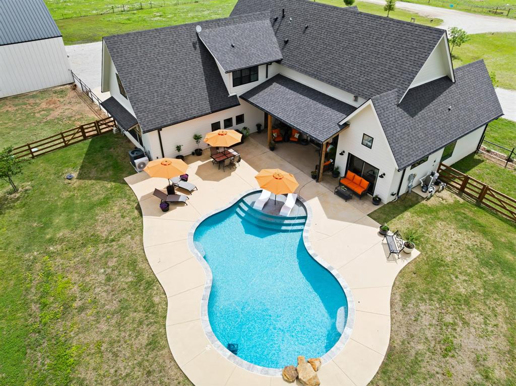 Nestled on beautiful acreage, this Texas farmhouse by Heritage Construction Group epitomizes the perfect blend of luxury, functionality, and wide-open space. As you enter, the expansive open-concept layout welcomes you with natural light and stunning views of the surrounding land. The great room boasts impressive hand-hewn beams and seamlessly transitions into a chef-inspired kitchen, featuring a 36-inch gas range, quartz countertops, an oversized walk-in pantry, and ample prep space.

This thoughtfully designed home includes 4 spacious bedrooms, 4.5 bathrooms, and a dedicated study with custom built-ins. The isolated primary suite serves as a private retreat, complete with a vaulted ceiling, shiplap accent wall, easy access to the back porch, and a large walk-in closet.

Upstairs, the versatile layout includes three additional bedrooms, a full bath, a second laundry room, a game room, and a bonus space, ideal for guests or multi-generational living.

Step outside to your enchanting covered back porch, perfect for relaxation and gatherings! The outdoor kitchen Area is equipped with both Gas and Electric hookups. This is ideal for barbecues or meals under the stars. Just steps away, the stunning inground pool, finished with PebbleTec, adds to the appeal. These features create a luxurious, resort-like atmosphere for unwinding or entertaining family and friends. Your personal paradise awaits!

A standout feature is the impressive 3,600 sq ft workshop, built with heavy-duty steel construction and equipped with electricity and water, and plumbed for septic. This space, which offers potential for living quarters or a barndominium, includes horse-ready Dutch doors and dedicated RV parking with 50-amp power. The shop is also fully insulated

Fully fenced and cross-fenced, the property is perfect for animals while maintaining a polished appearance. More than just a home, this property represents a lifestyle of luxury, land, and limitless possibilities.